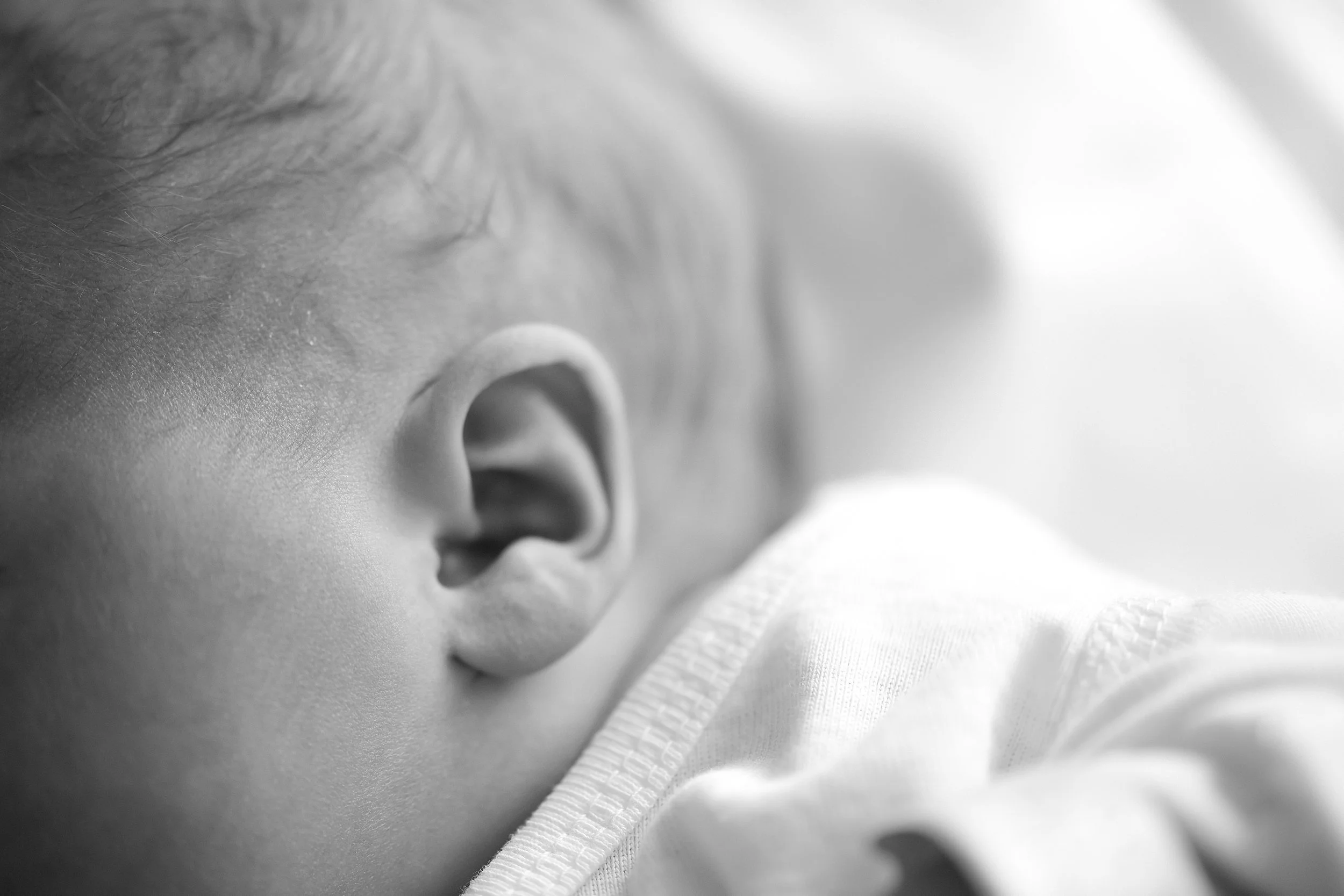 Close-up of a baby's ear and part of the face, with soft lighting and blurred background.