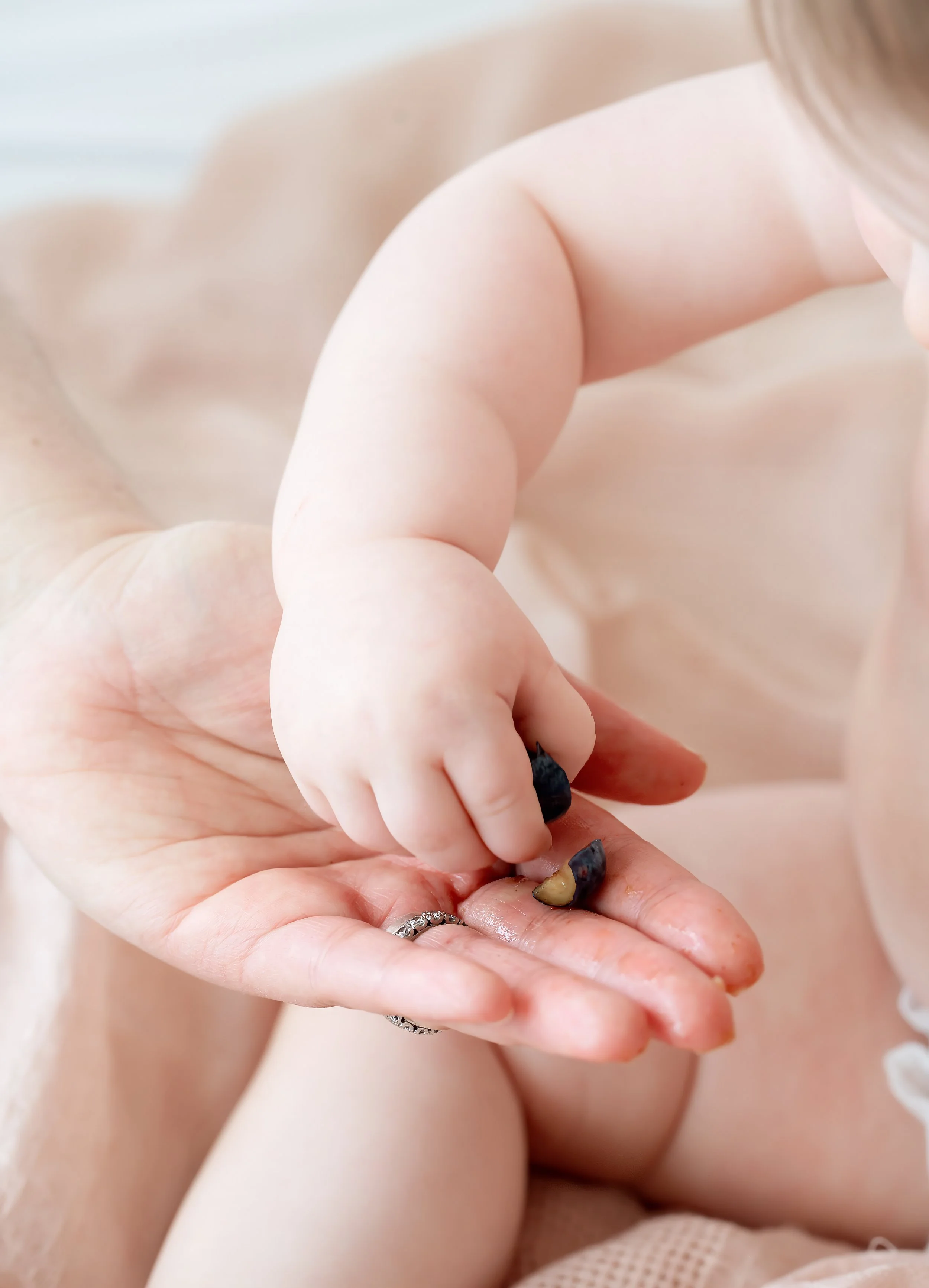 Close-up of a mother holding her baby's tiny hand, focusing on their hands and a tooth in the mother's palm.
