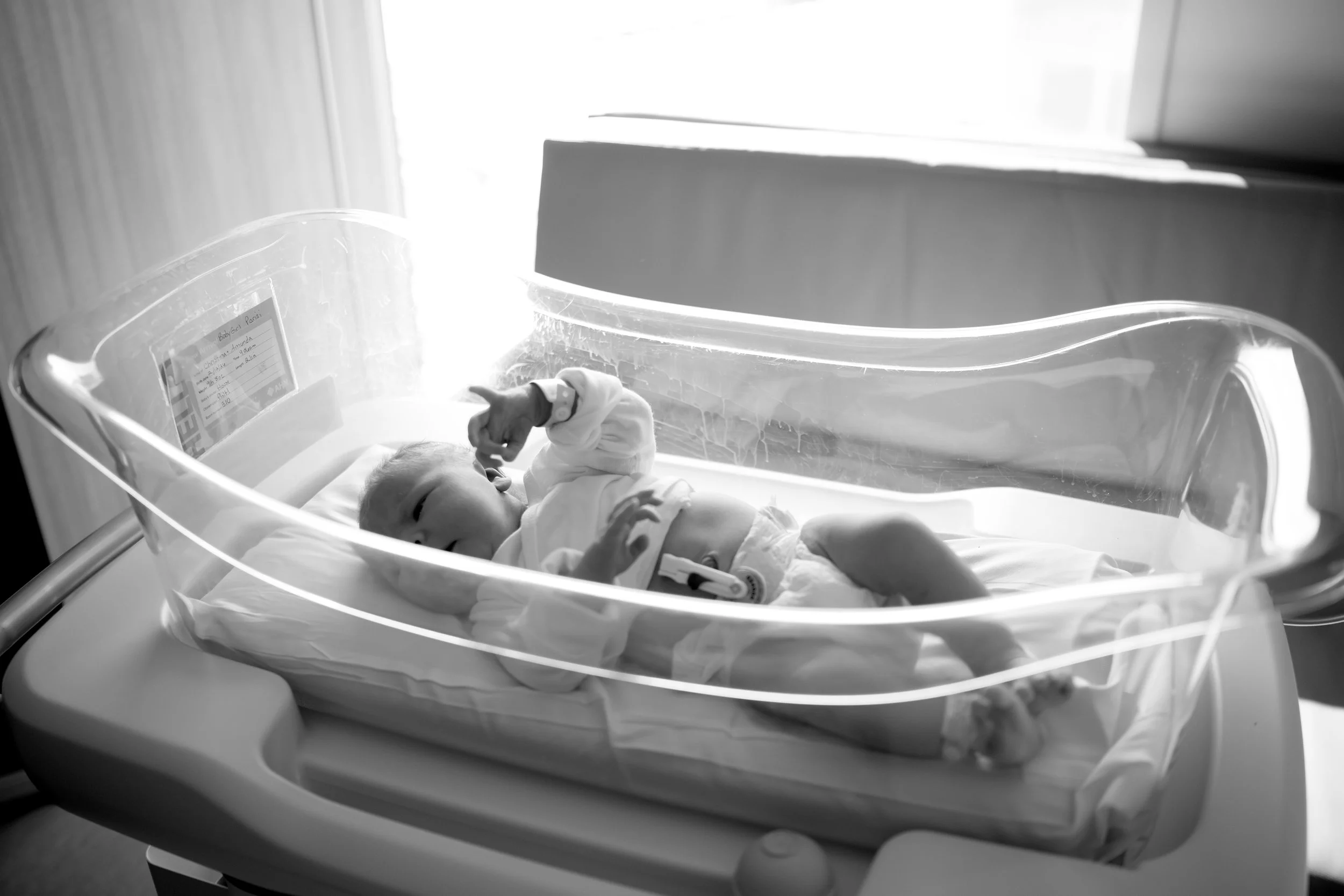 A newborn baby lying inside a hospital crib in a medical setting.