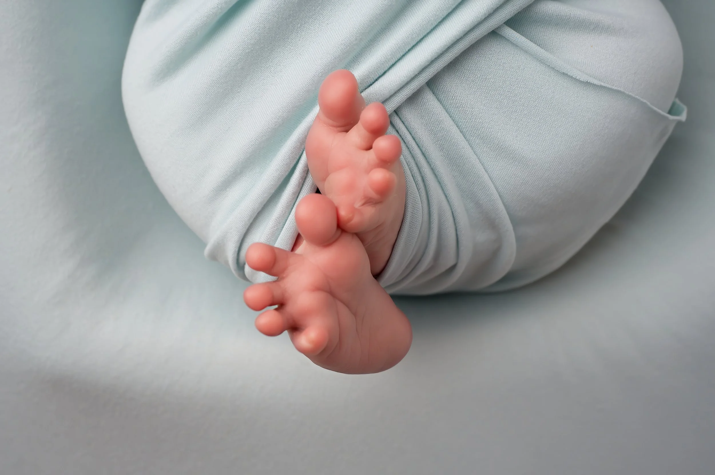 Close-up of a baby's tiny hand grasping an adult's finger, with the baby wearing light-colored clothing.