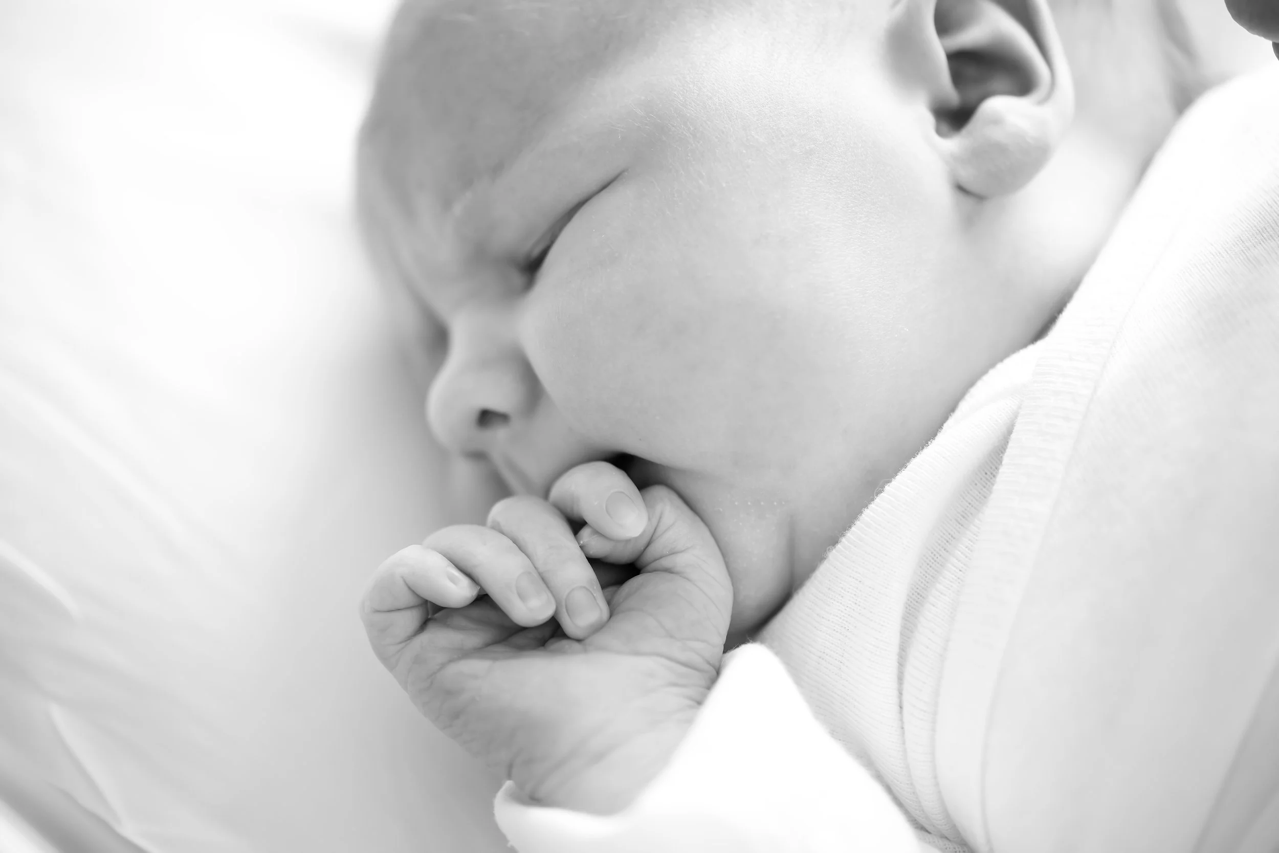 Close-up of a newborn baby's face with a hand gently touching the baby's chin in black and white.