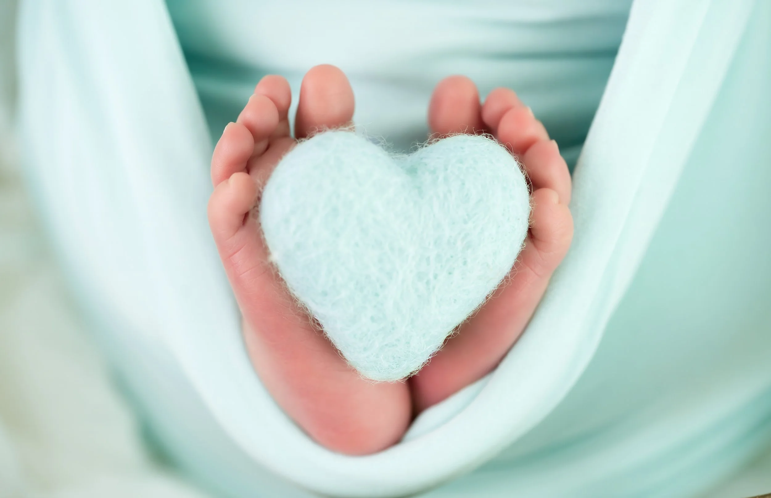 A person in a light blue shirt holds a small, plush, light green heart-shaped object in their hands.