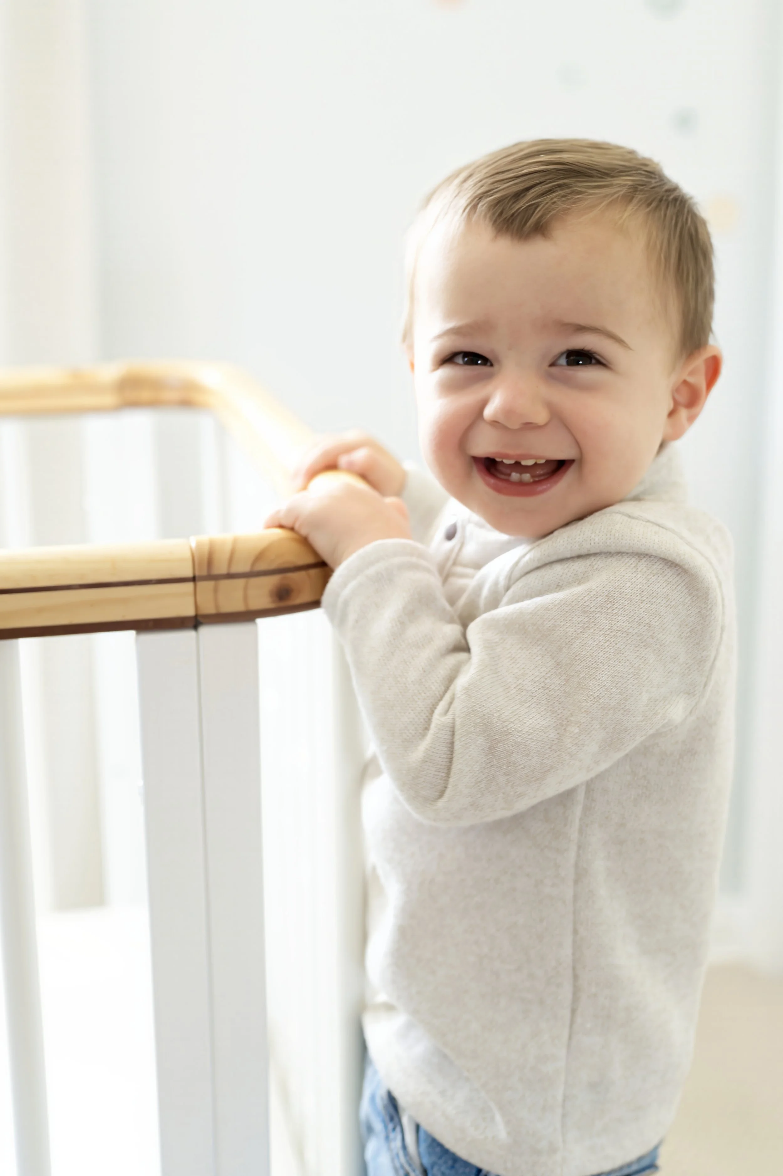 A young boy with short brown hair smiling while holding onto a wooden railing.