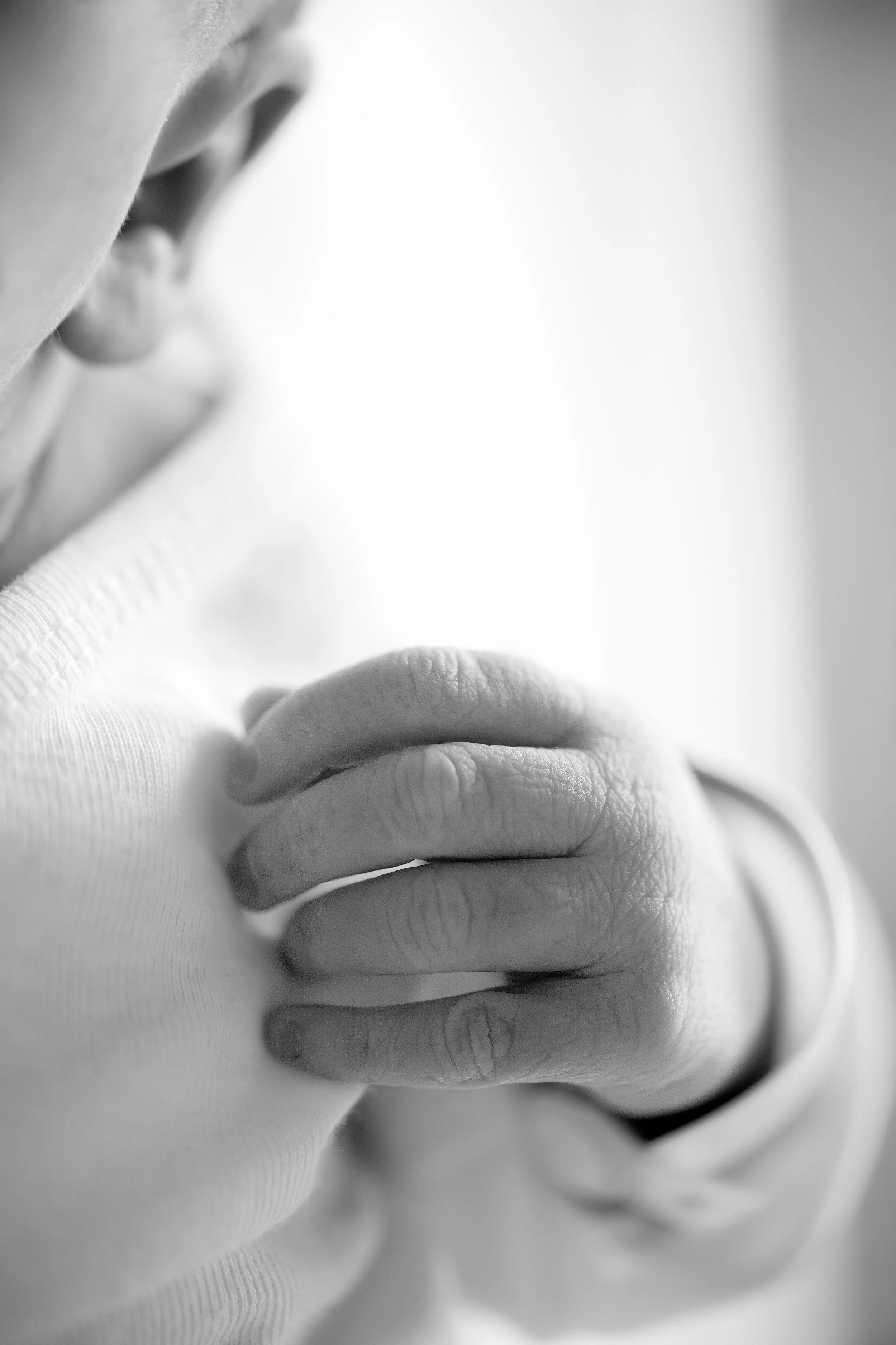 Close-up black and white photo of a newborn's hand and ear.