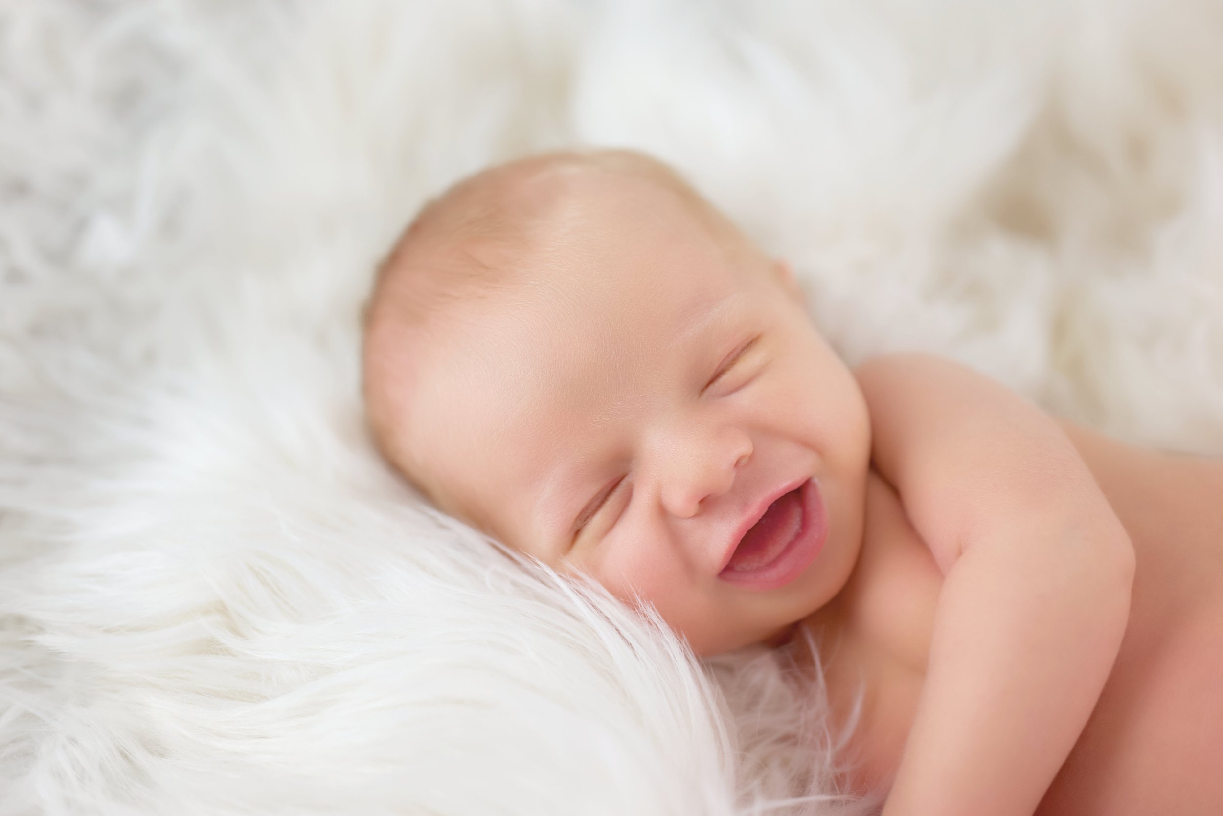 Smiling newborn baby sleeping on soft white blanket.