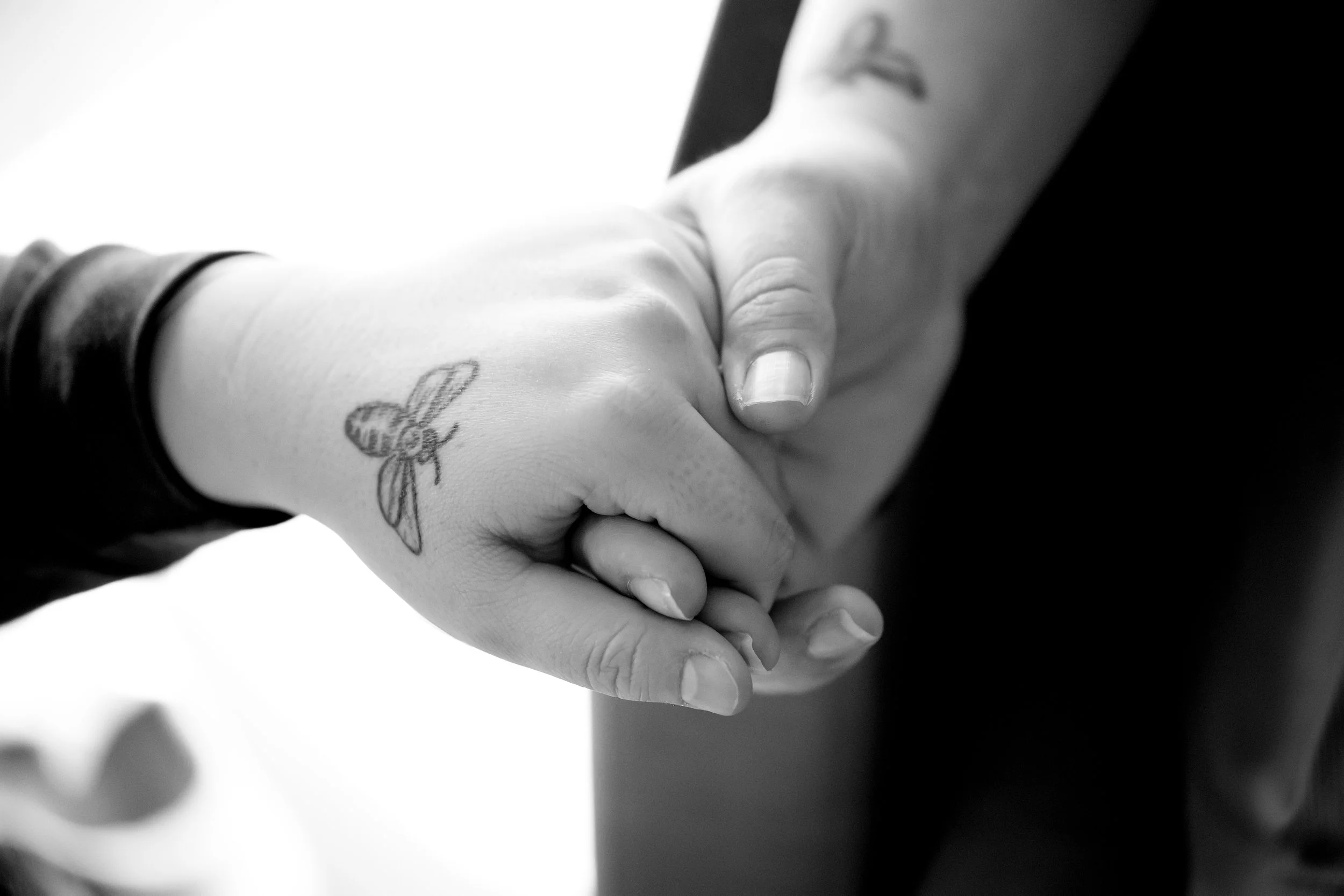 Close-up of two people holding hands, both with a tattoo of a bee on the wrist.