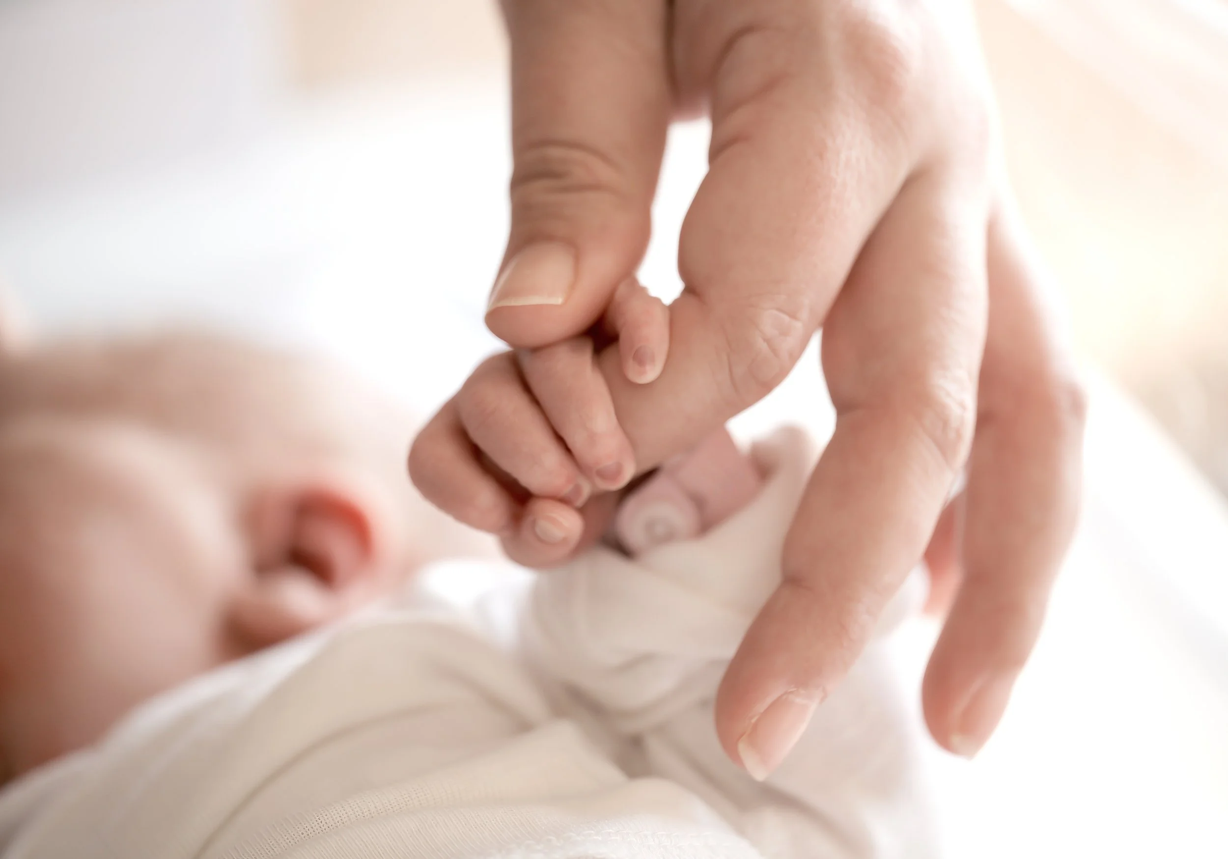 Close-up of a baby holding an unseen adult's finger.