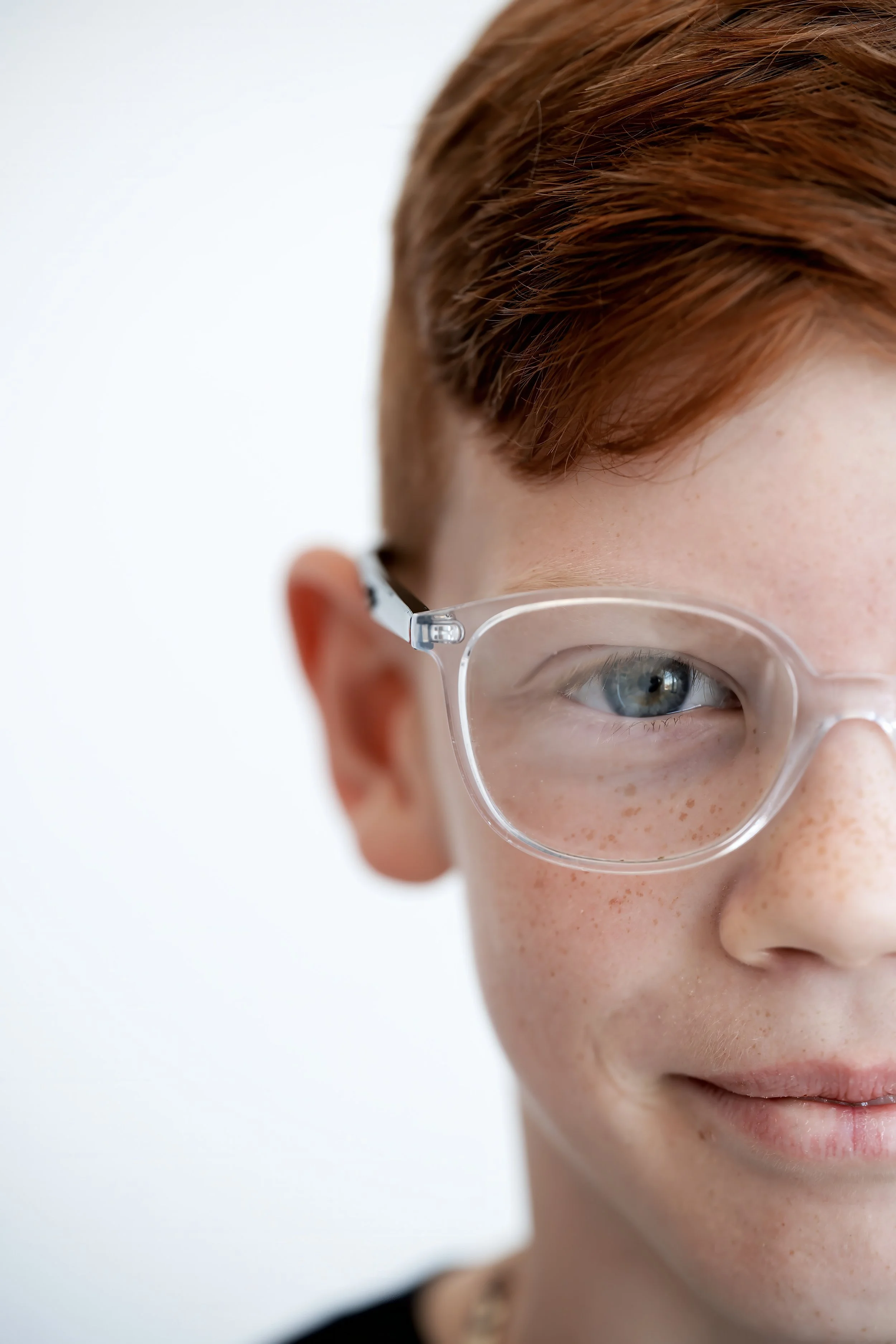 Close-up of a young person with red hair, glasses, and freckles against a plain white background.