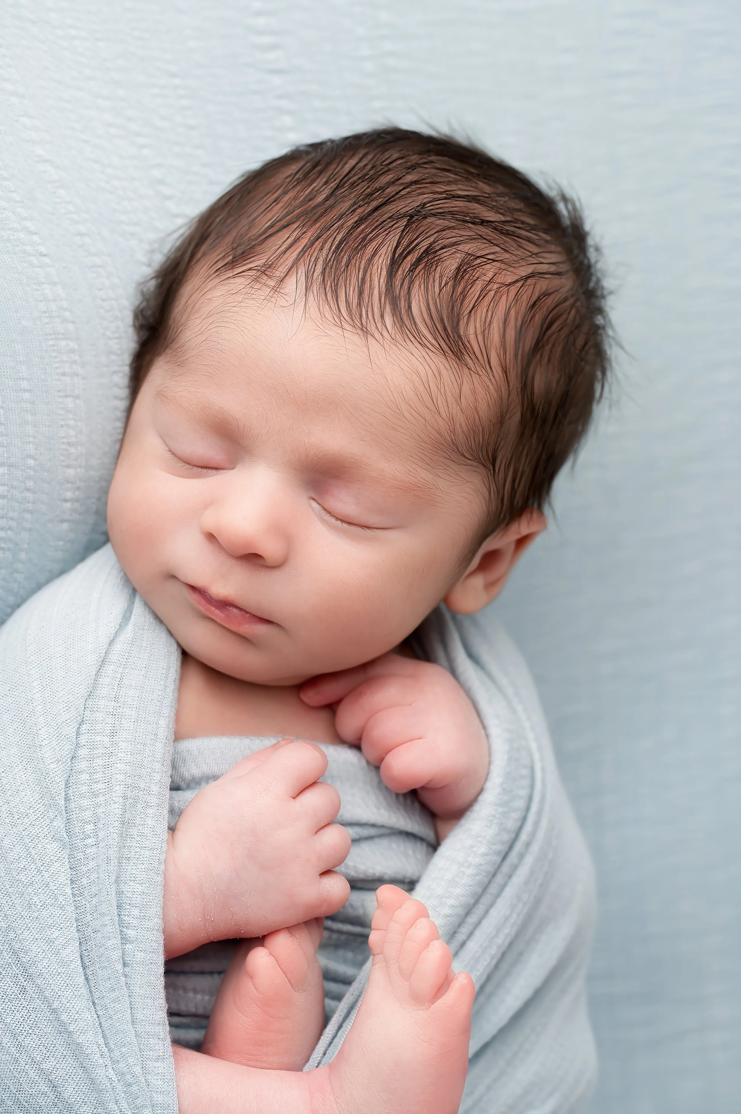Close-up of a sleeping newborn baby with wet hair, gently cuddling a tiny doll.