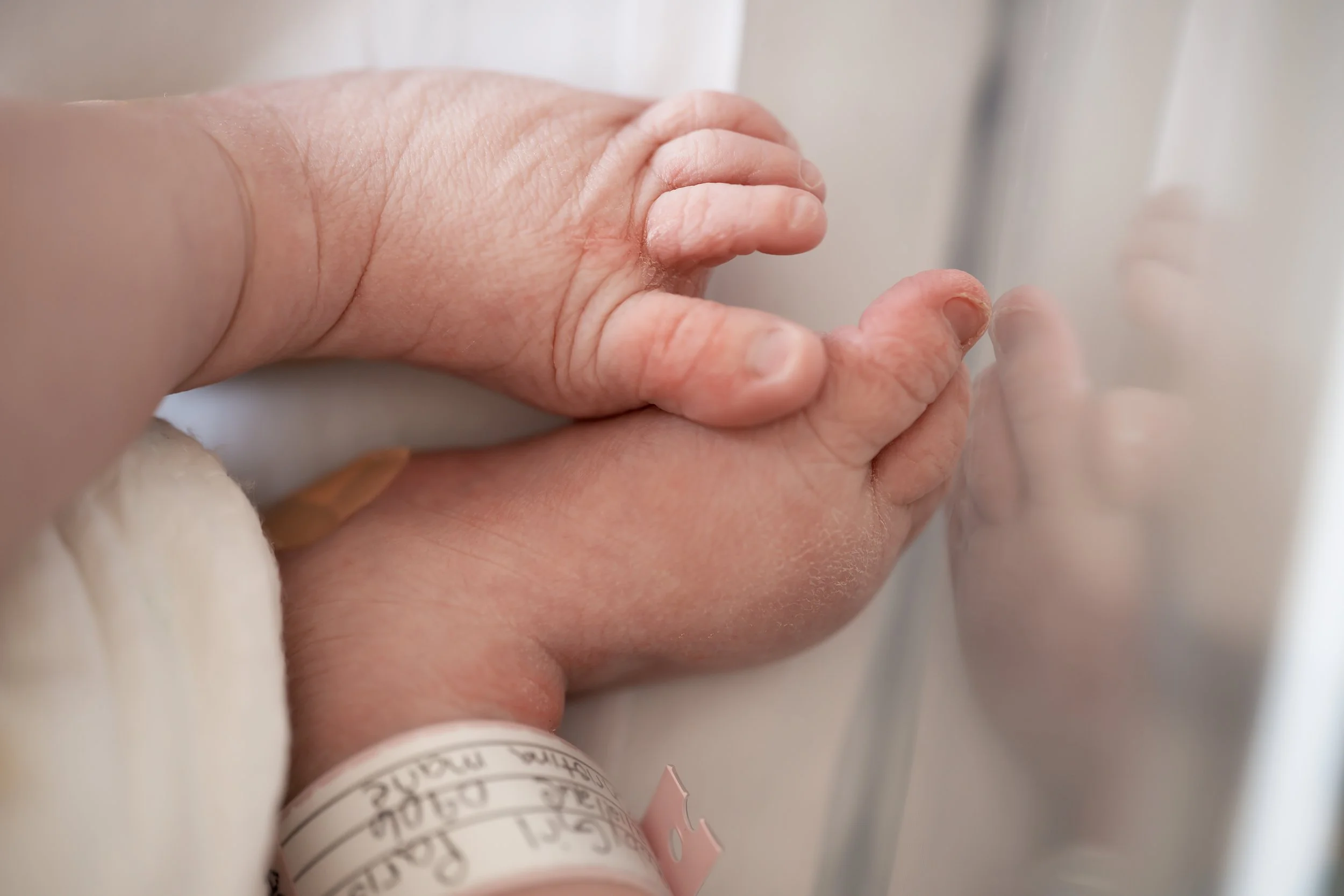 Close-up of a newborn baby's feet against a hospital crib, with part of a hospital bracelet visible on the baby's ankle.