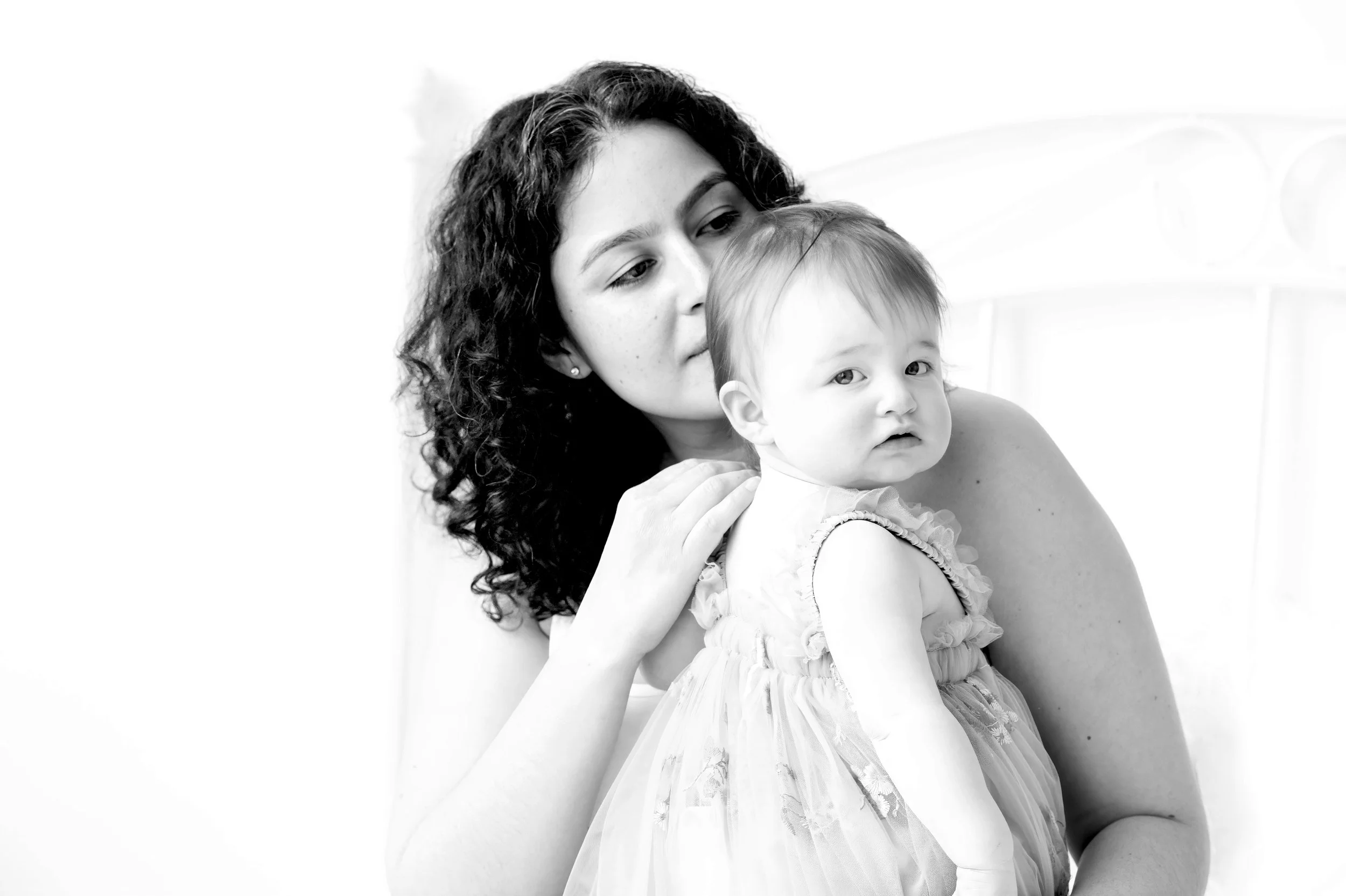 Black and white photo of a woman with curly hair holding a young girl, both looking softly at each other.