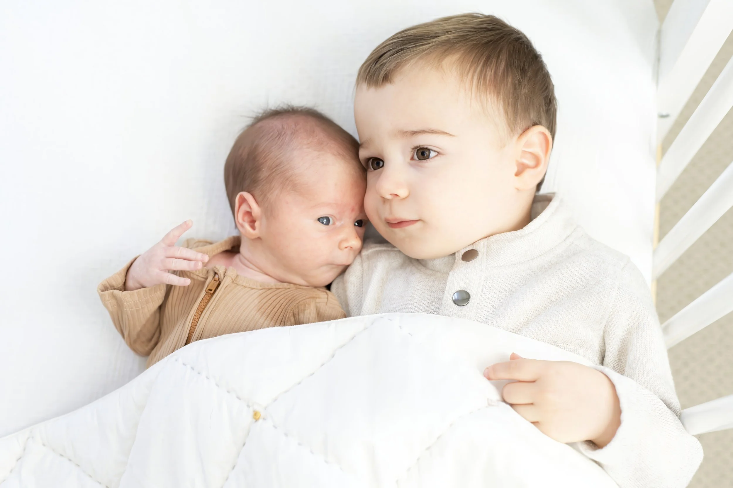 A young boy lying in bed with a newborn baby, they are close together, indicating a sibling relationship.