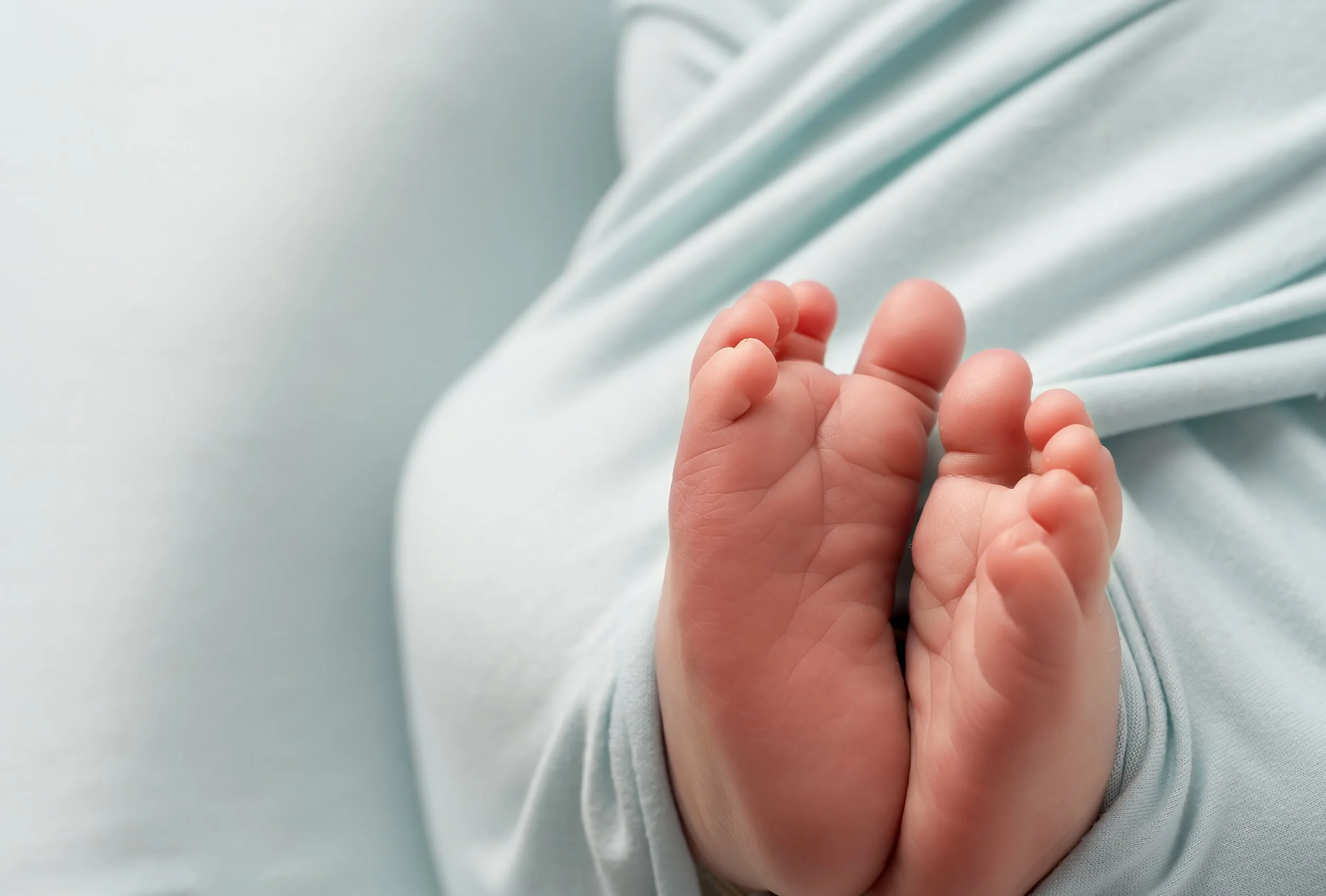 Close-up of a small baby's hand grasping an adult's finger, with both hands resting on a soft, light-colored fabric background.