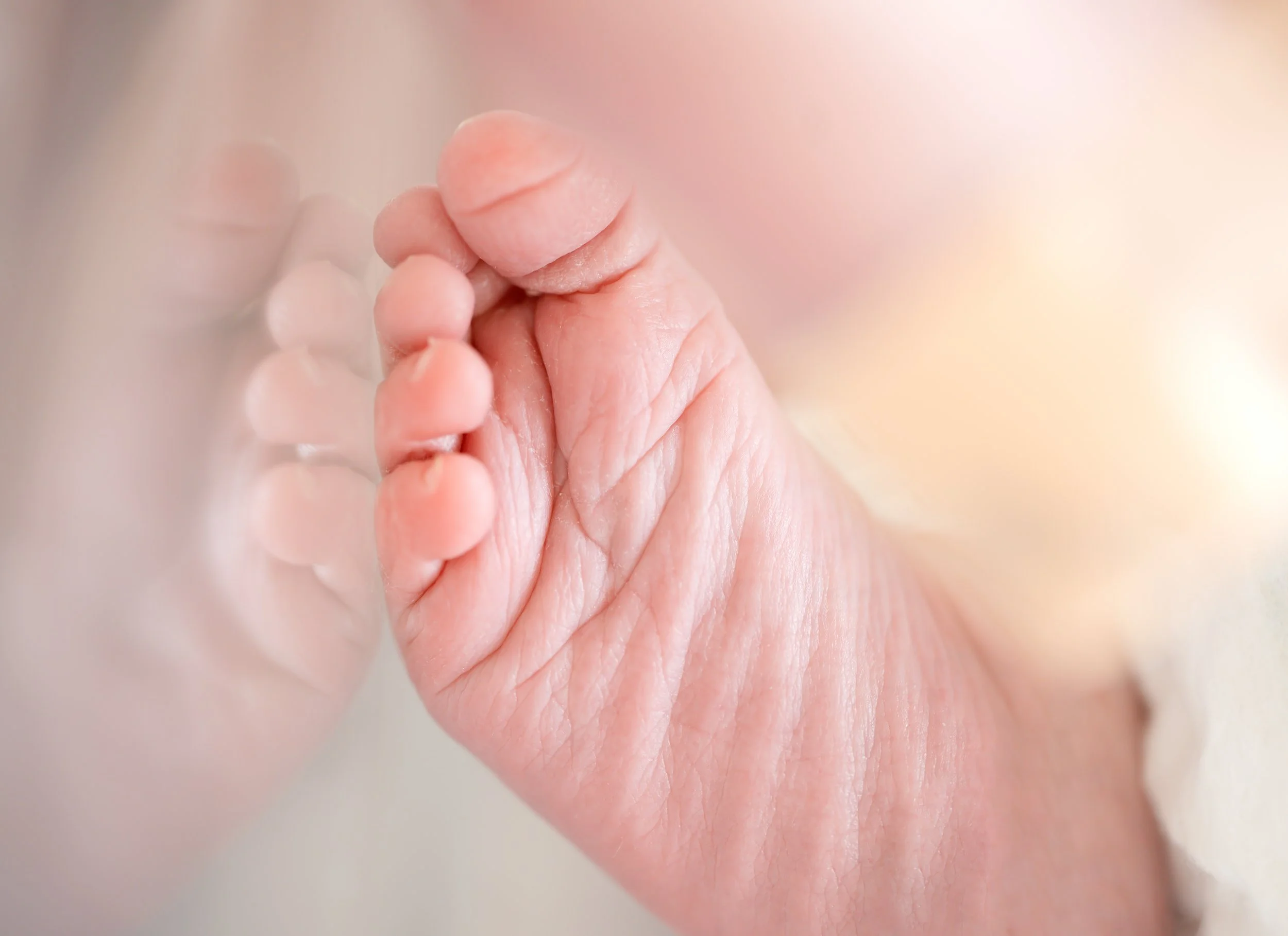 Close-up of a baby's foot resting against a hospital crib. A soft reflection can be seen.
