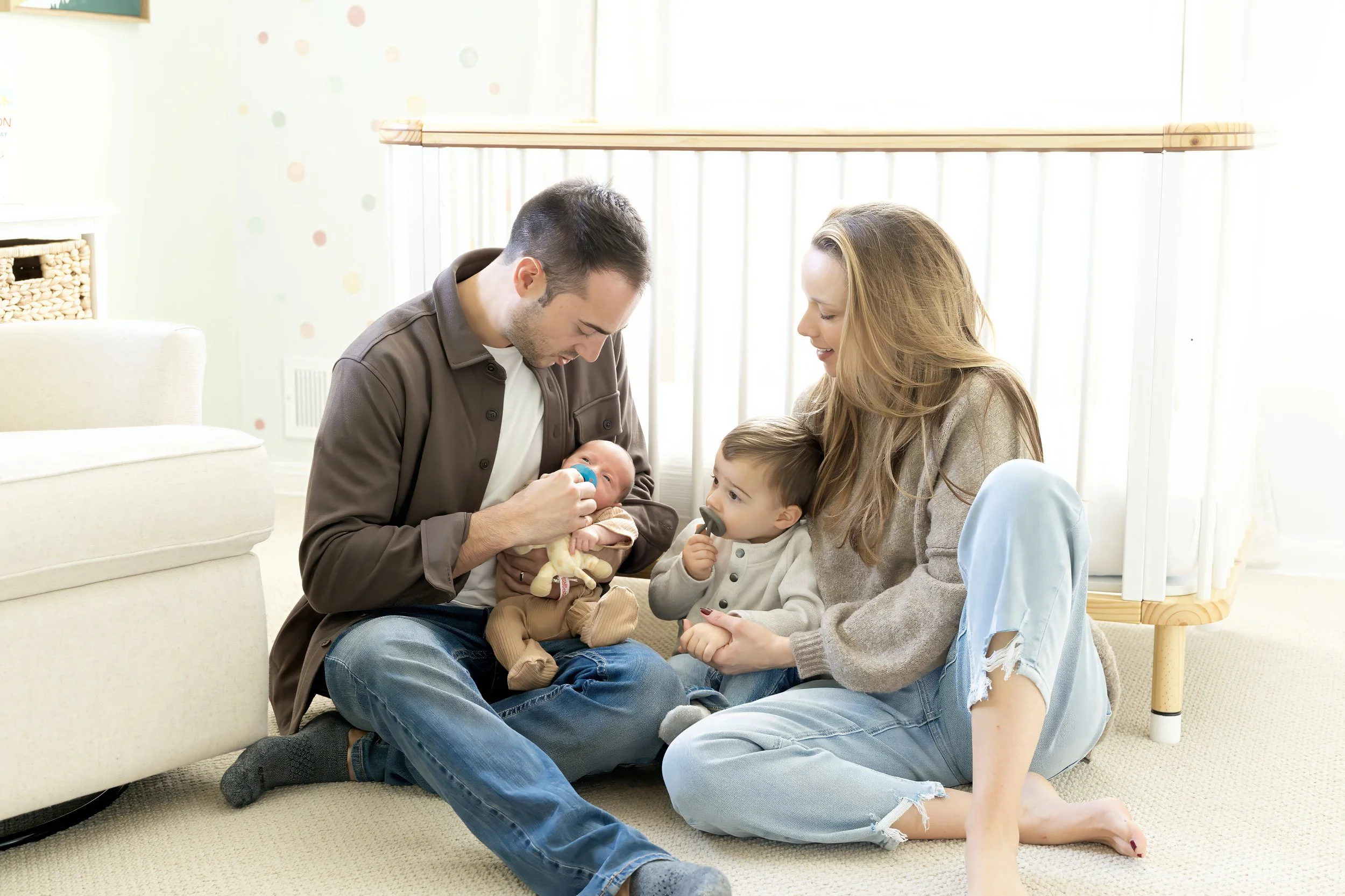 Family with two children sitting on the floor, interacting with a baby.