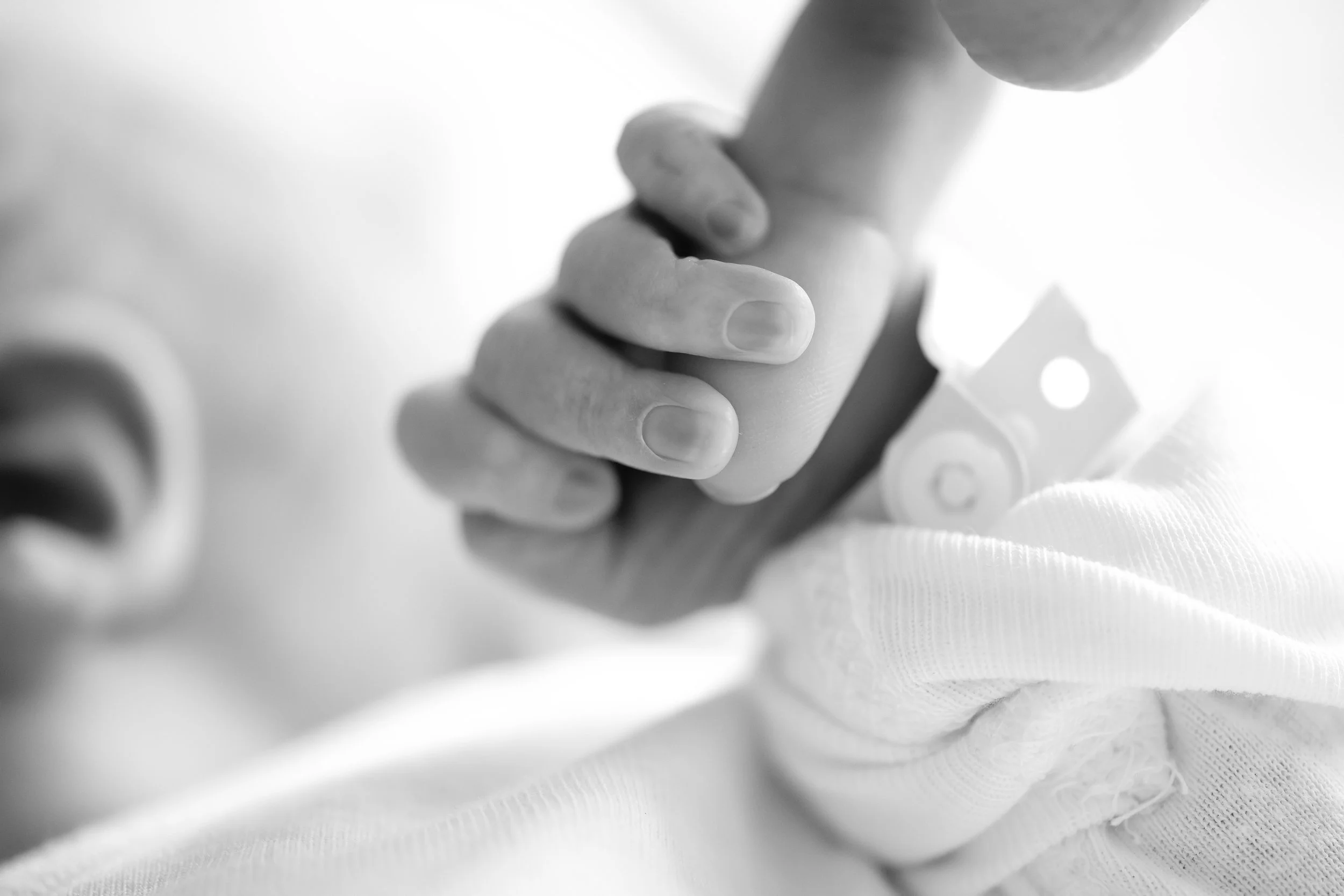 Close-up of a newborn baby's hand gently holding an adult's finger while wearing a white long-sleeved shirt.