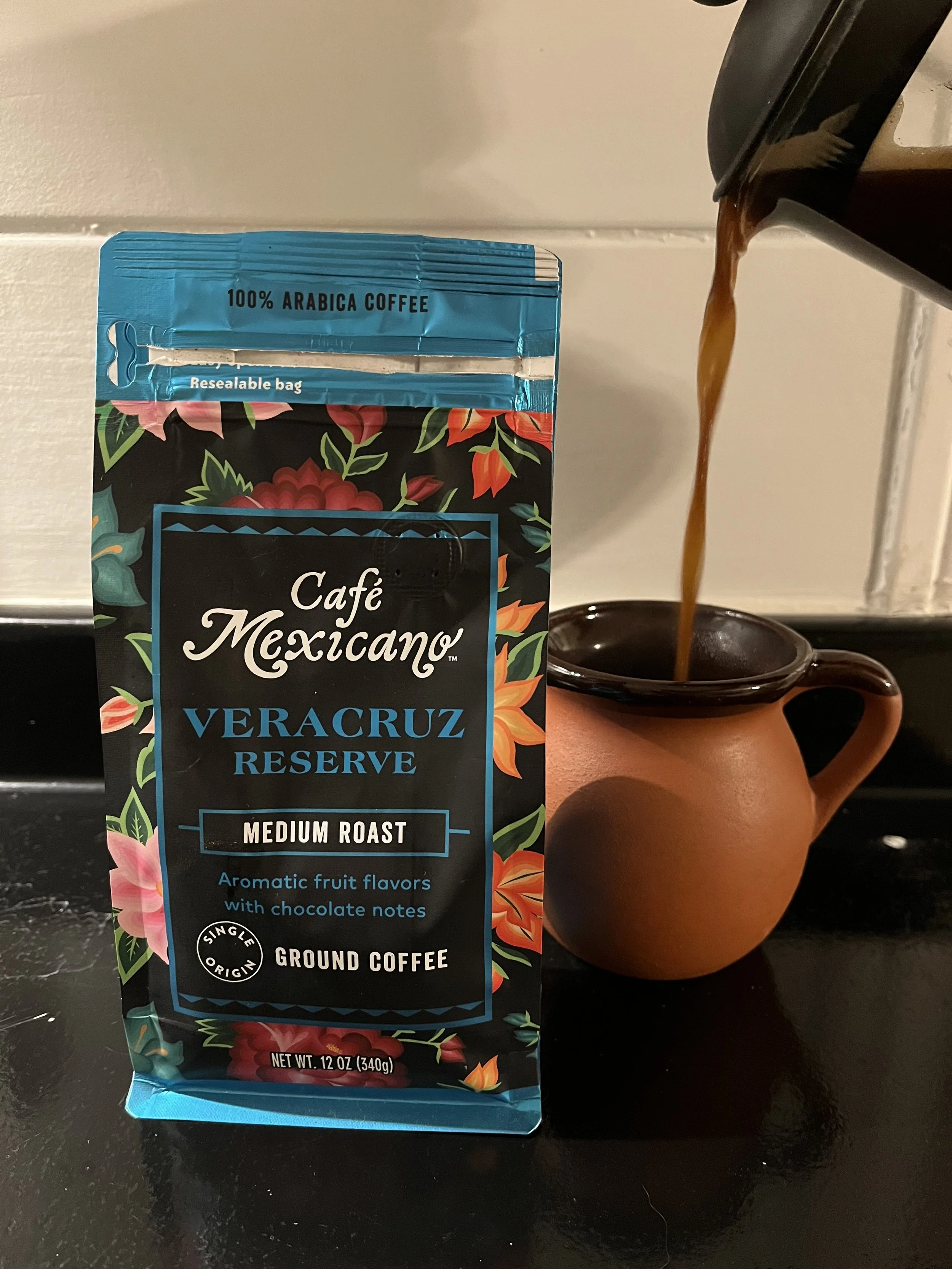 bag of Café Mexicano coffee in front of a cup with coffee pouring into it