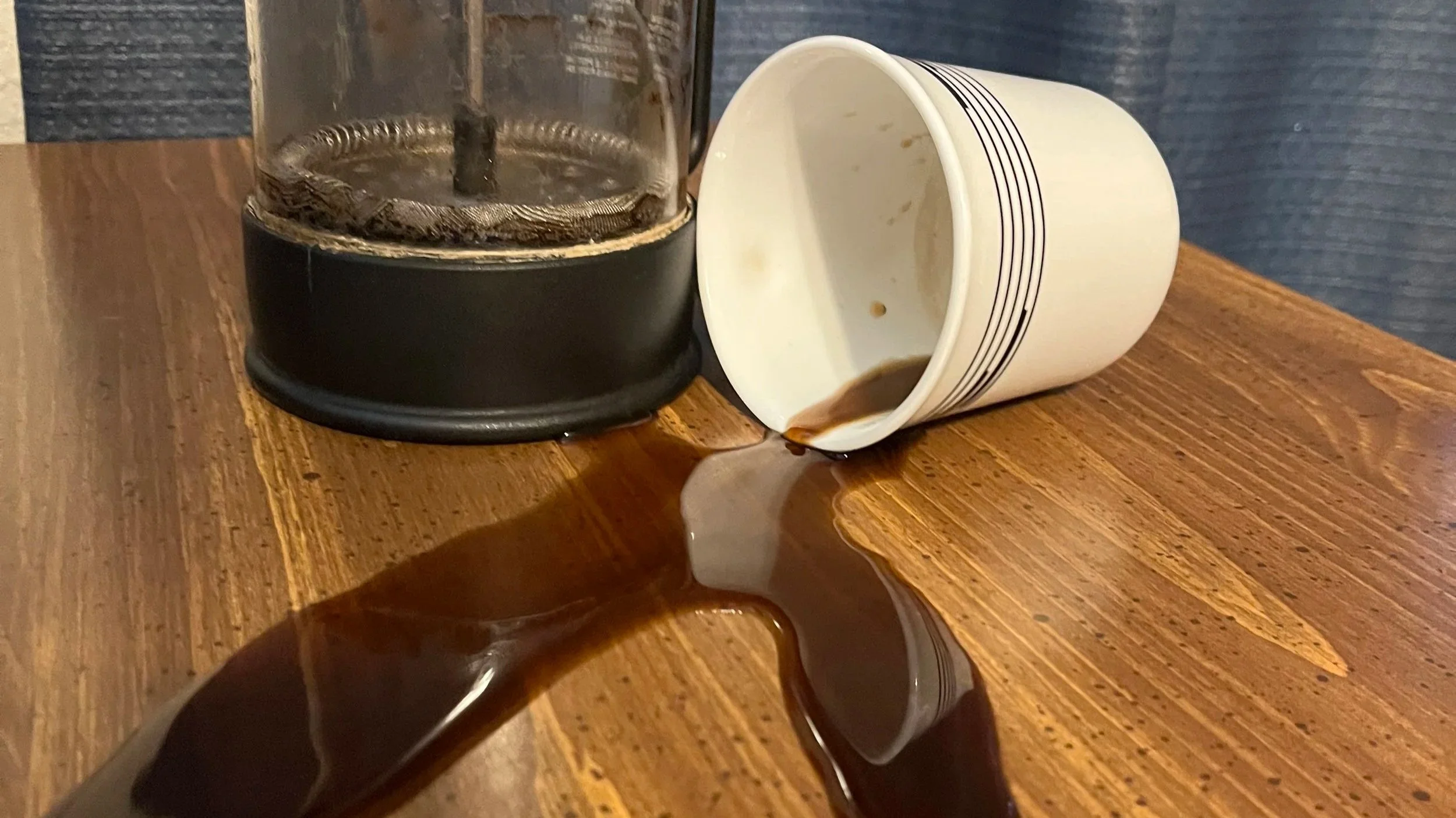spilled coffee next to a turned over mug and a french press
