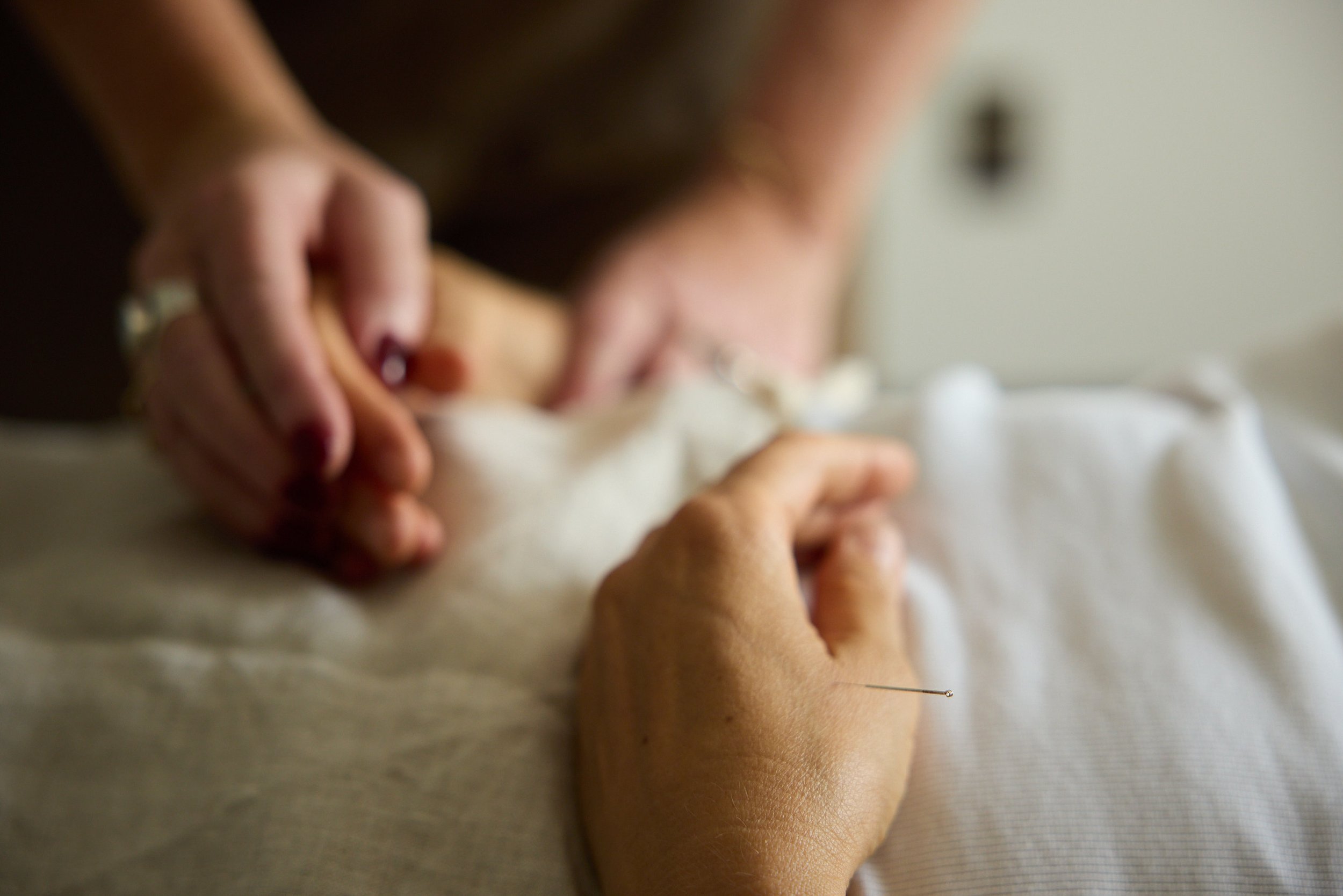 Close-up image of a person's hand holding scissors cutting fabric or paper, with a blurred background.