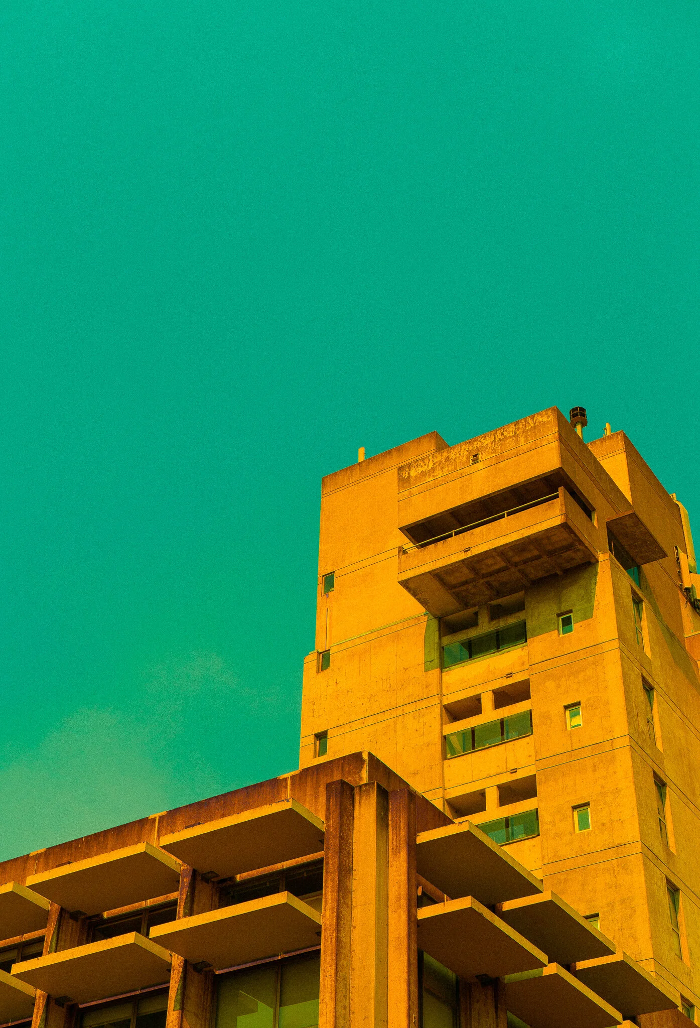 A yellowish beige multi-story building with balconies and large windows under a clear blue sky.