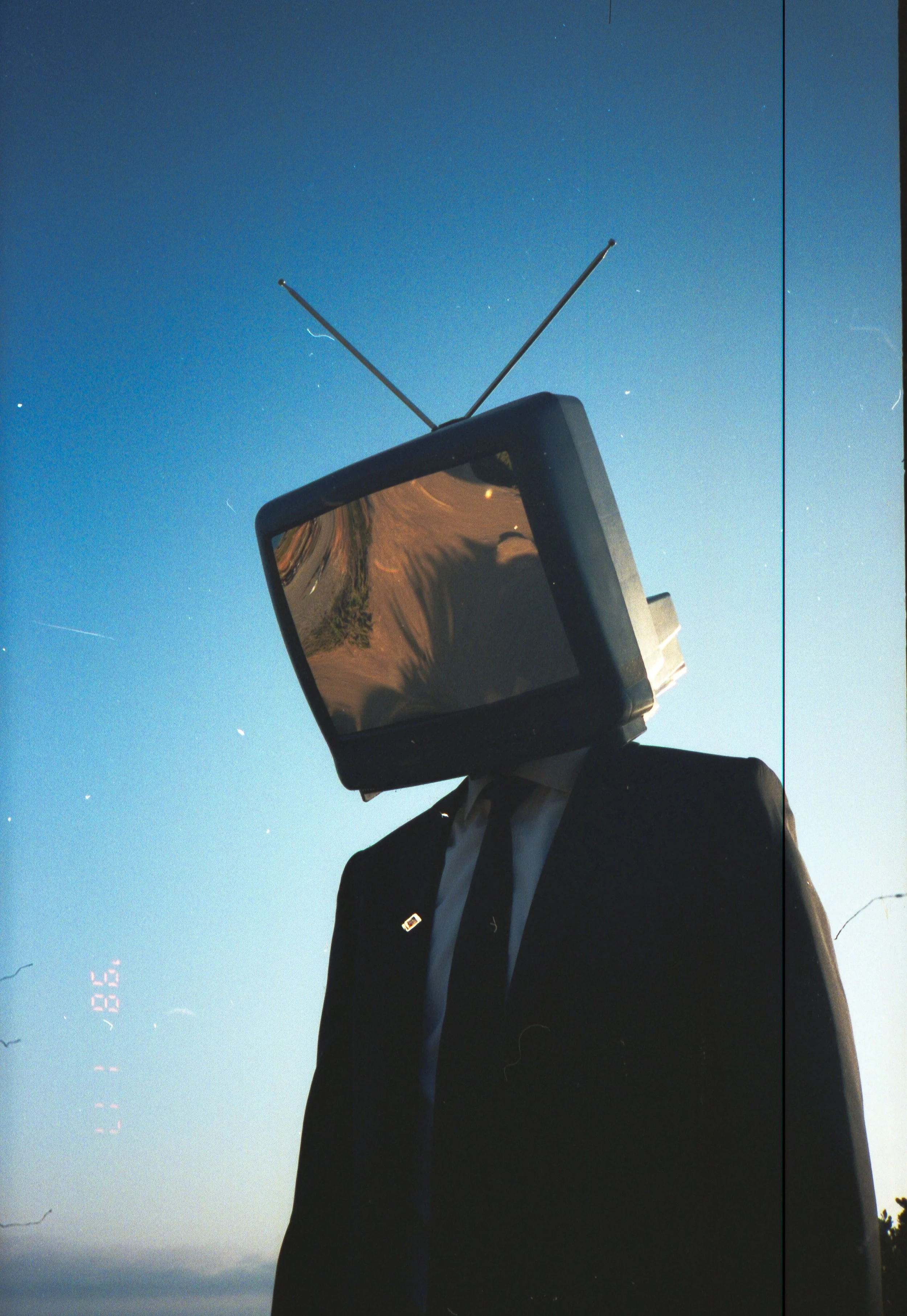 Person wearing a suit with a television for a head, standing against a blue sky with some clouds.
