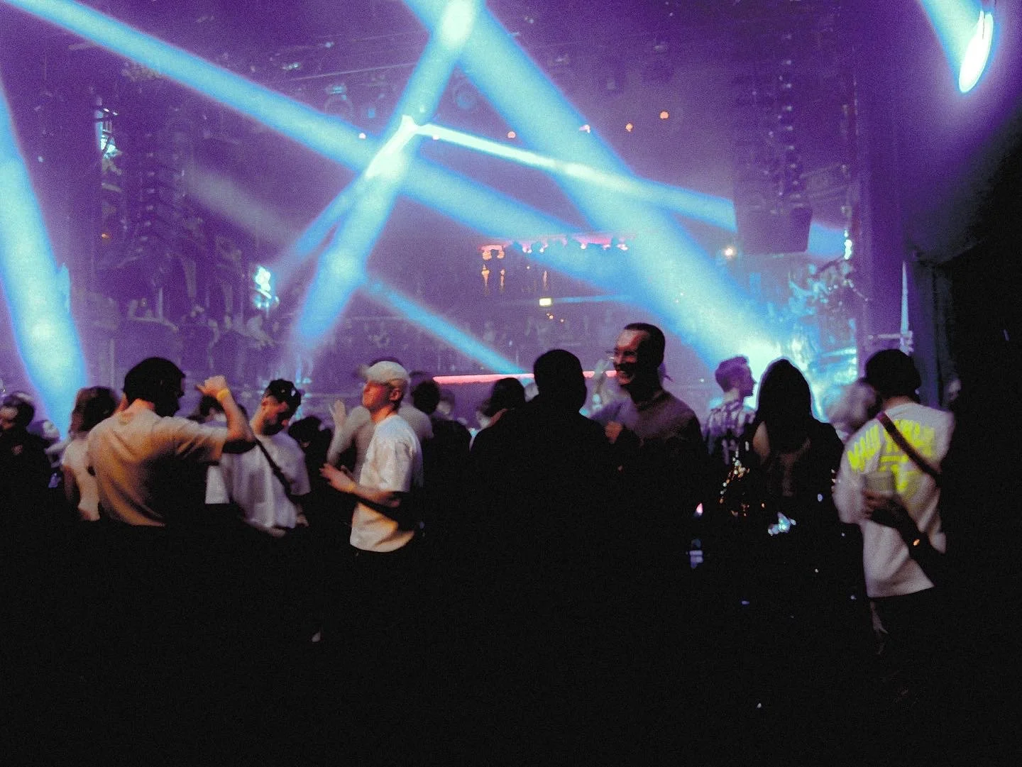 People dancing at a nightclub with bright blue and purple lights and a DJ booth in the background.