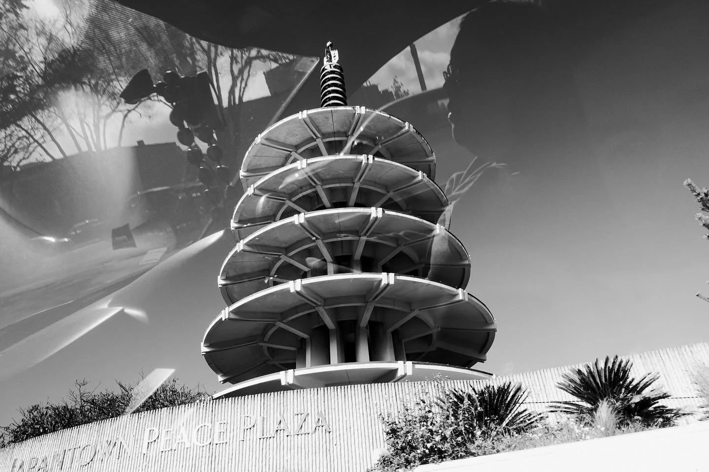A reflection in a mirrored surface showing a multi-story tower with a spiral slide, and trees and sky in the background.