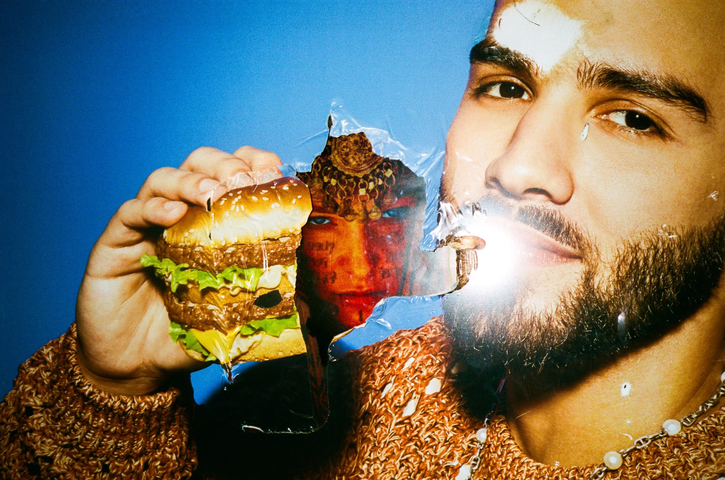 A person holding a large burger with lettuce, tomato, and a patty, while a photo of rebecca ferguson, as the Bene Gesseritt is seen in the background.