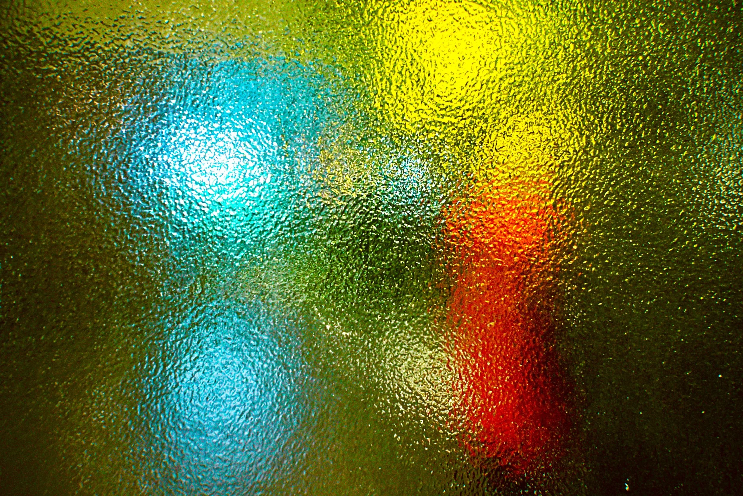 Close-up of raindrops on a glass window with colorful lights in the background, creating a vibrant pattern.