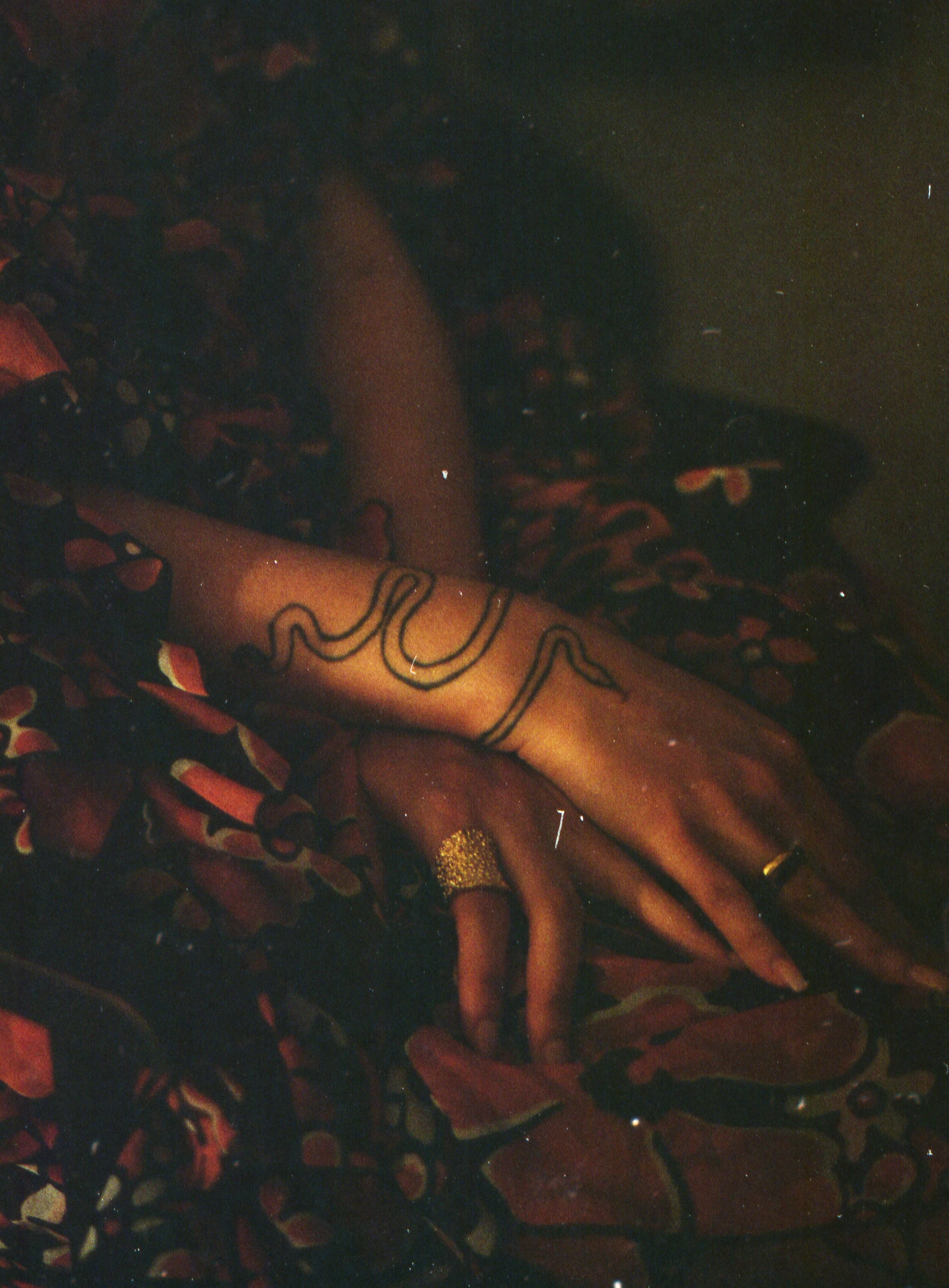 Close-up of a person's arm resting on a floral-patterned fabric, with tattoos and jewelry visible.