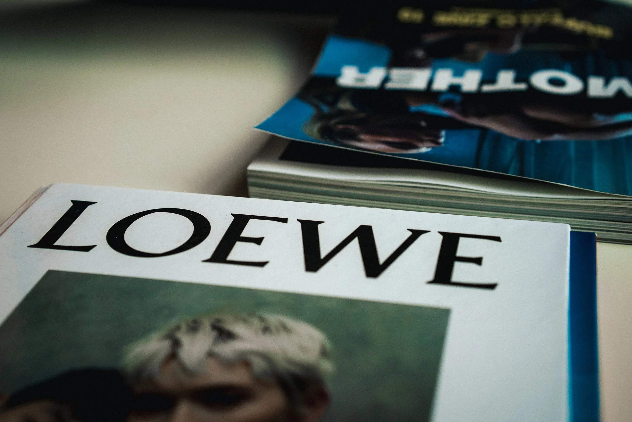 Close-up of a magazine with the word 'LOVE' on the cover, placed next to a book with the title 'MOTHER' and a partially visible magazine featuring a dog and the word 'WATCHER' in bold letters.