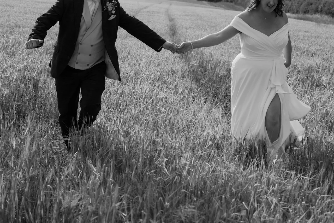 Black and white close-up of bride and groom running through a field at their Ed’s Hill Top Tent marquee wedding in Stamford