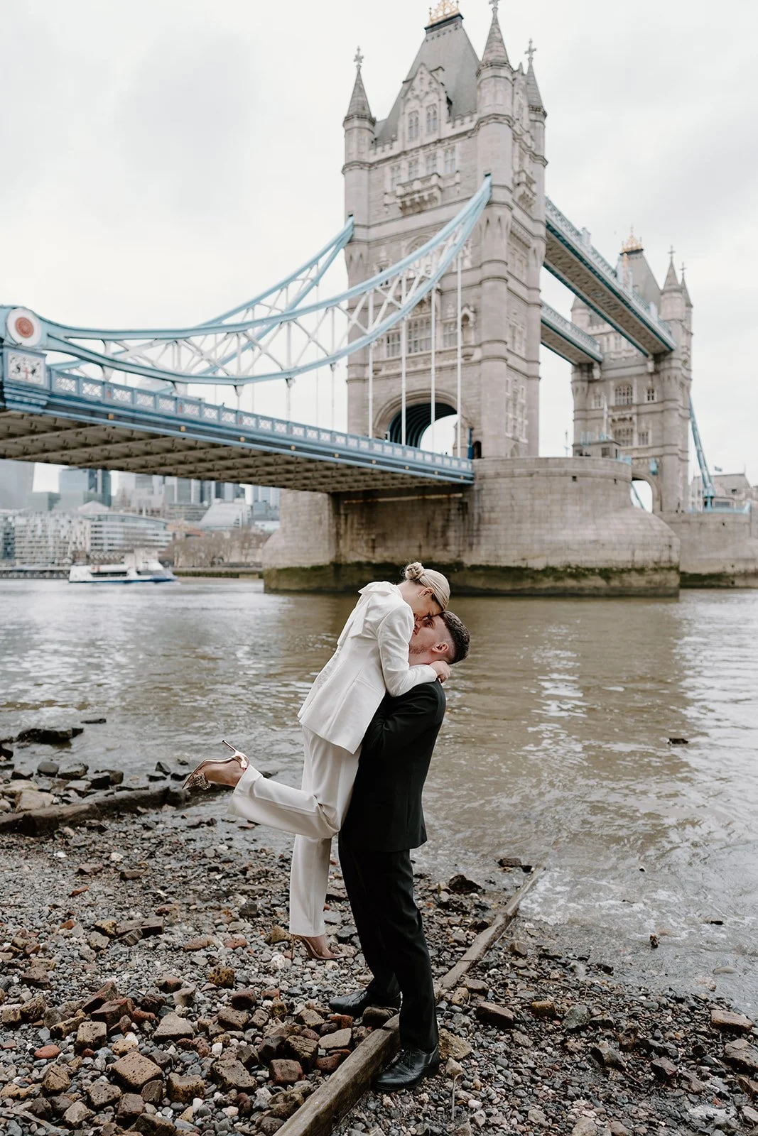 Groom lifting his bride in a white suit by Tower Bridge, London city wedding photography