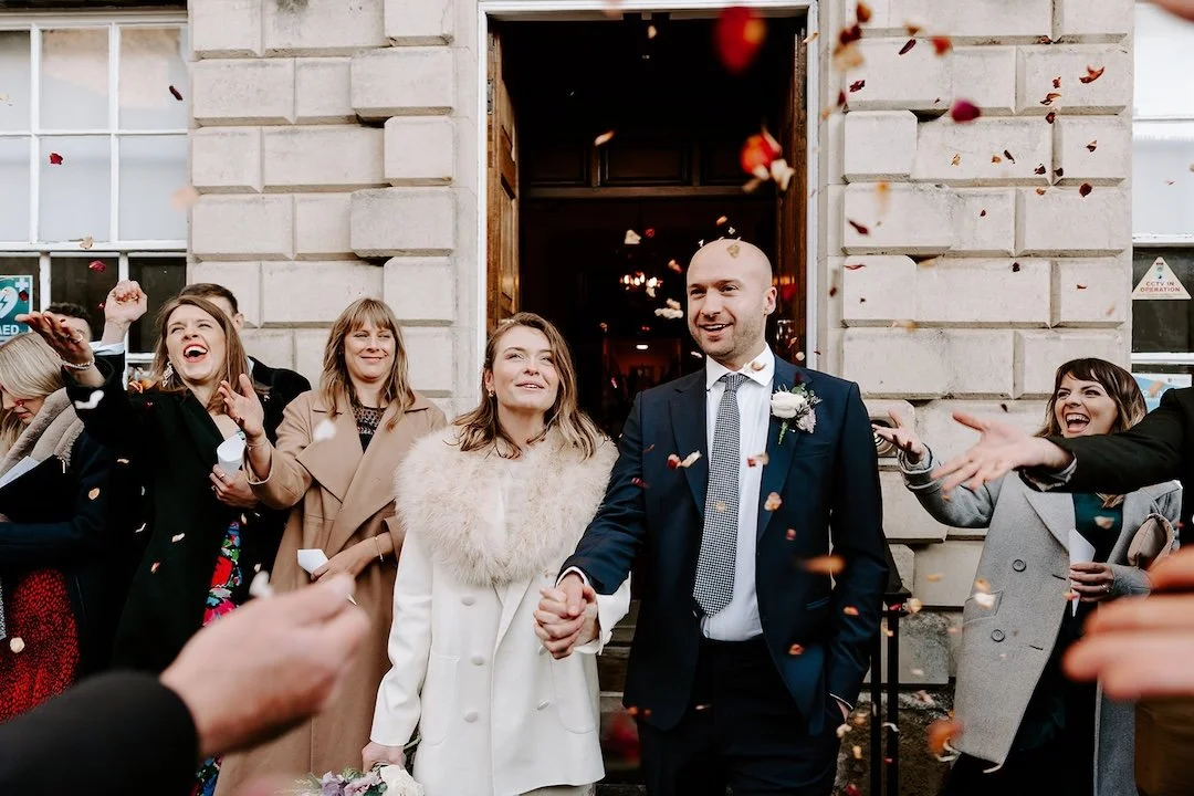 Newly married couple walking out of Stamford Town Hall as guests throw confetti.