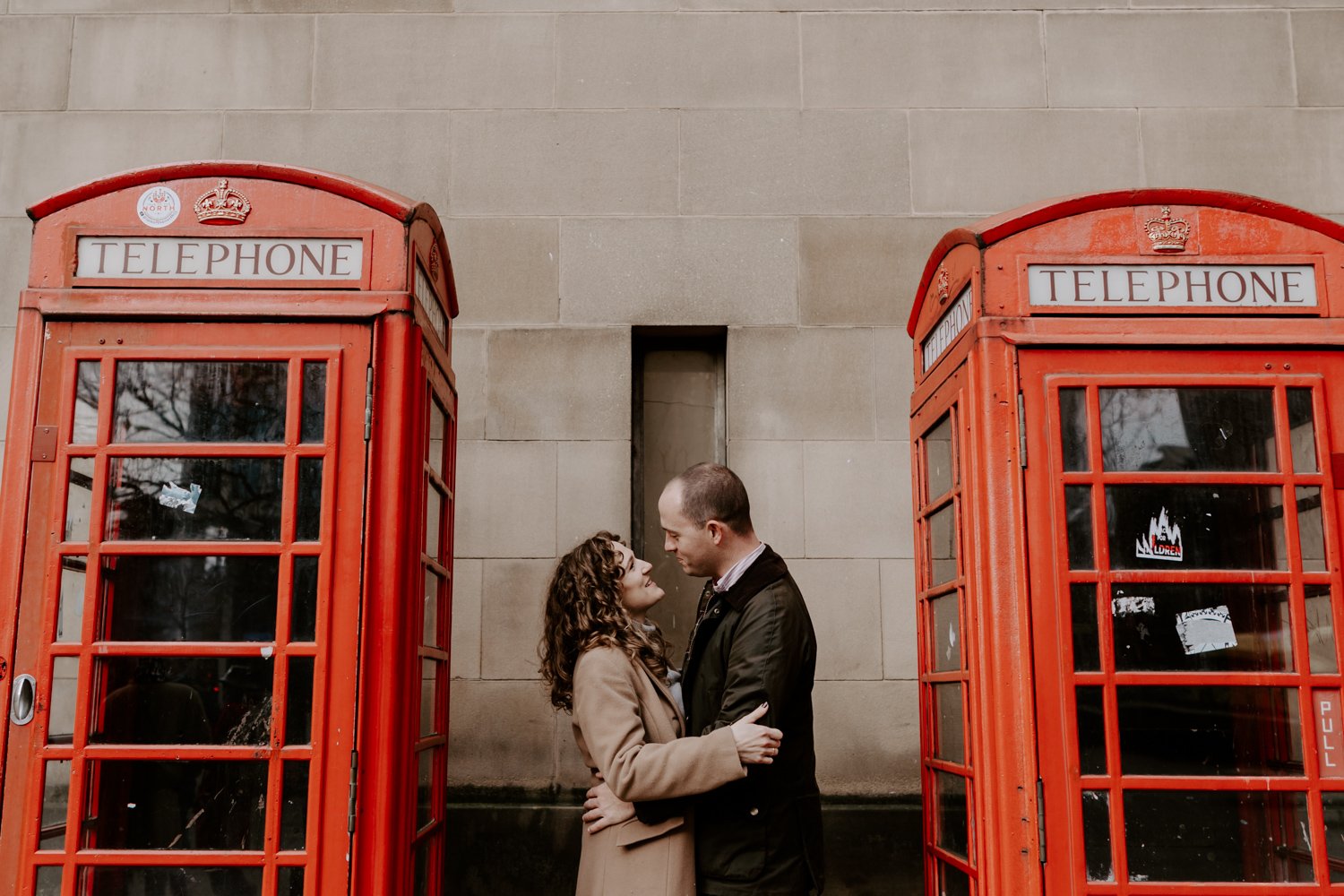 couple standing embracing inbetween two red phoneboxes Manchester pre-wedding photoshoot