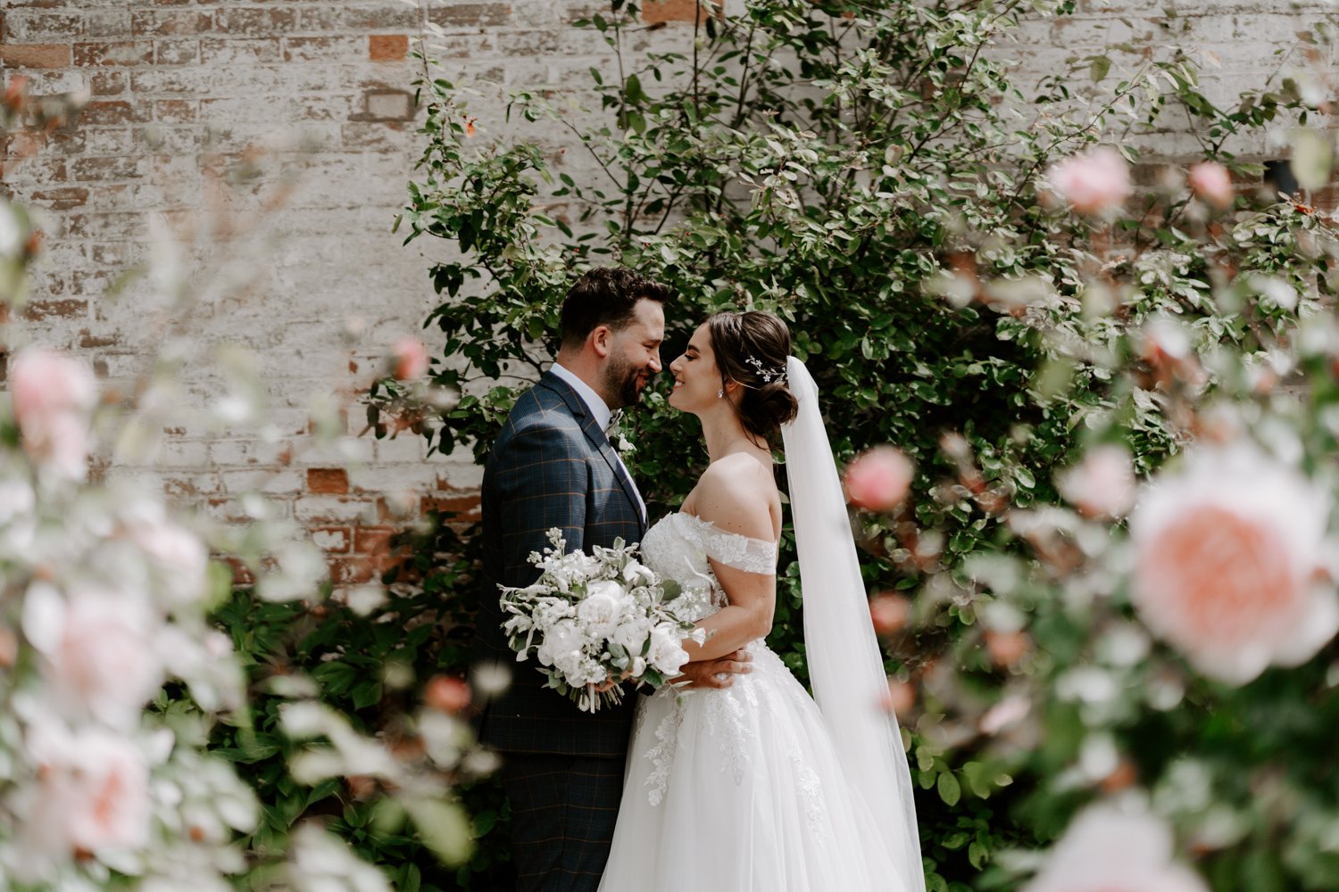 bride groom smiling looking at each other amongst rose bushes Bassmead Manor Barns wedding 