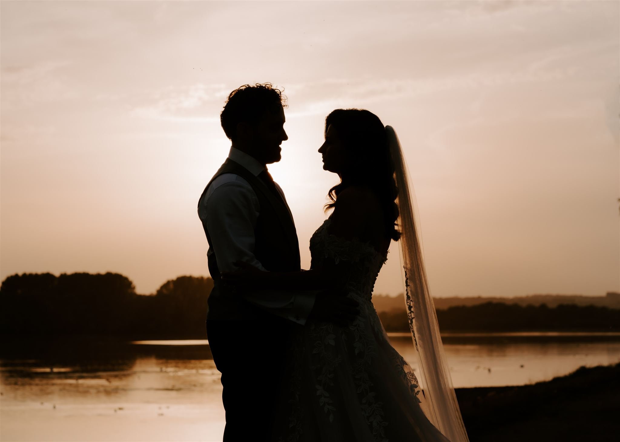 bride and groom silhouetted against sunset sky during golden hour