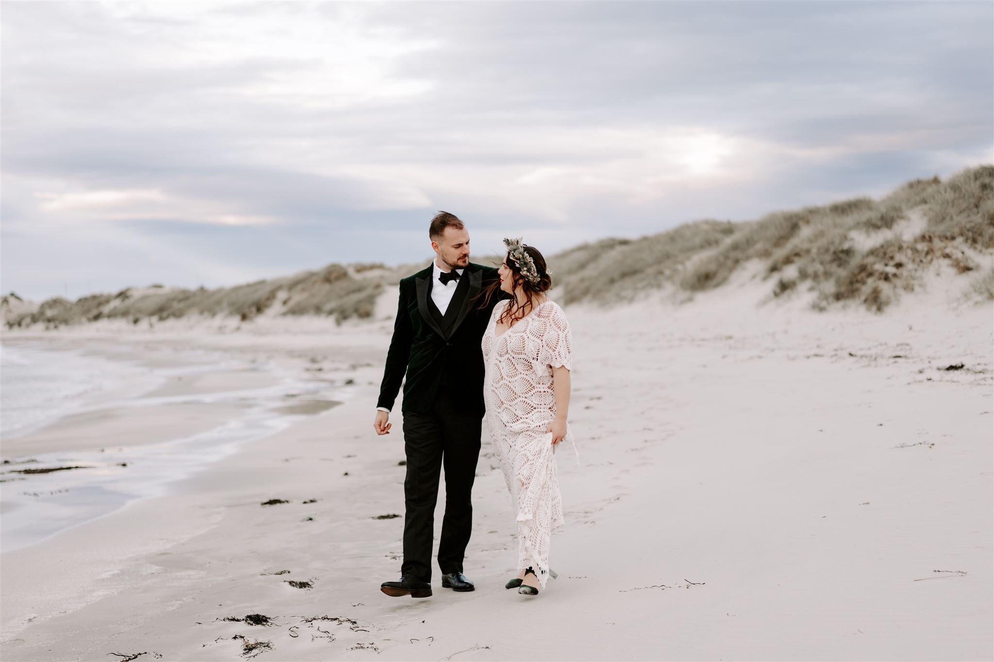 bride groom walking arm in arm on beach during sunset and golden hour