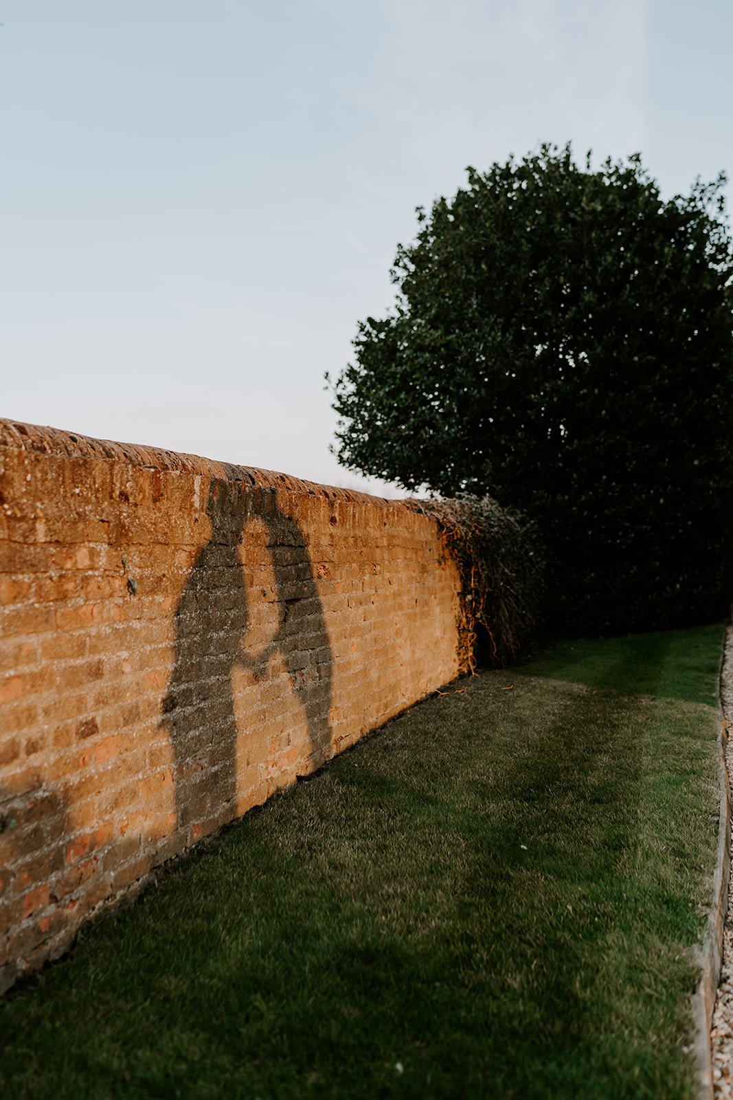 shadow of bride and groom kissing on stone brick wall during golden hour
