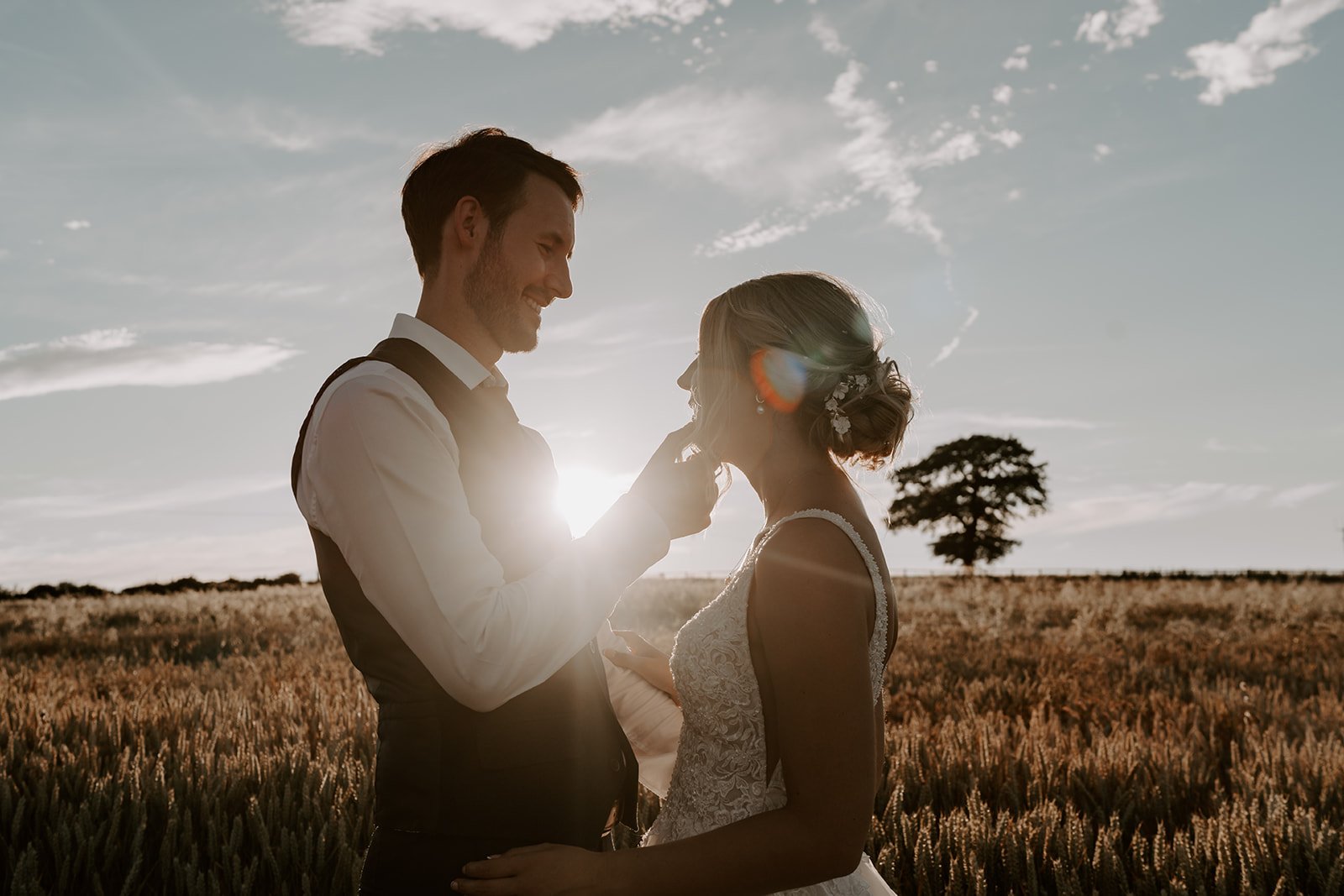 groom tucking brides hair behind ear during golden hour with sun shining and setting behind them