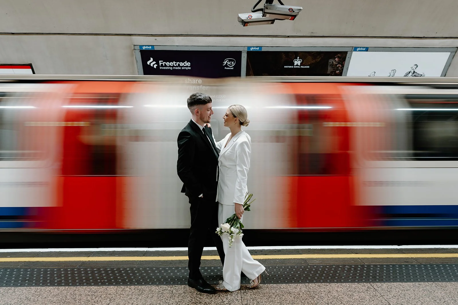 Bride and groom standing on a London Underground platform as a train passes, modern city wedding photography