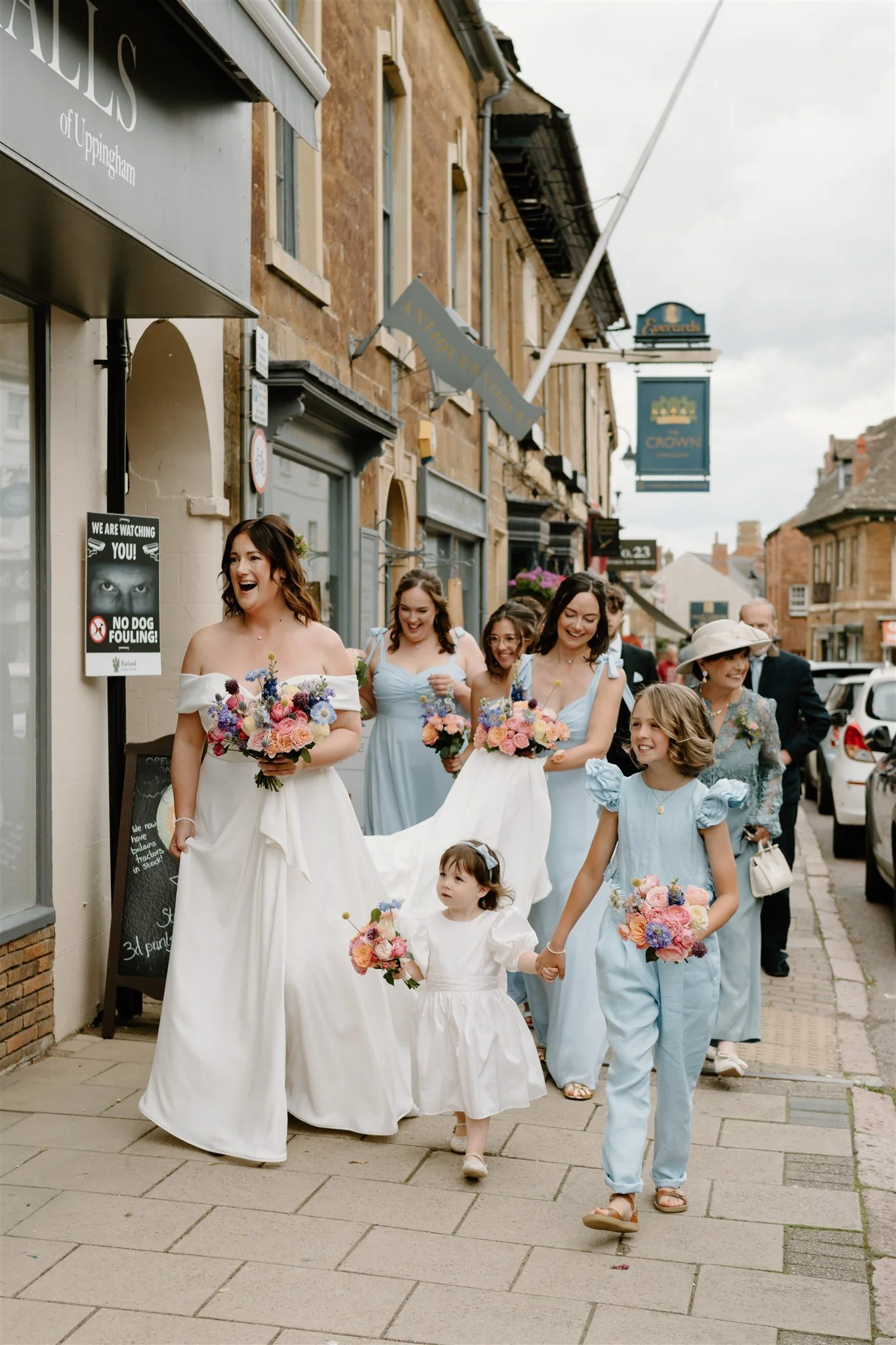 Documentary style photograph of a bride, bridesmaids and flower girls walking through a market town street on the way to the wedding ceremony, natural wedding photography in Rutland.