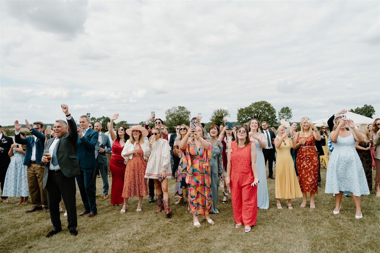 Wedding guests cheering and filming the hot air balloon launch at Ed’s Hill Top Tent marquee wedding in Stamford
