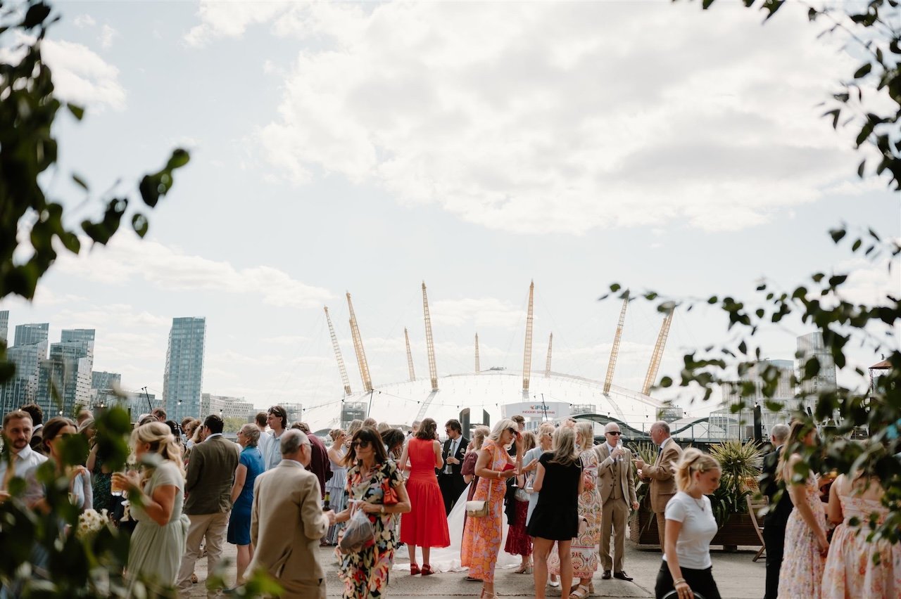 Wedding guests socialising on the riverside terrace of Trinity Bouy Wharf with the O2 Arena in the background