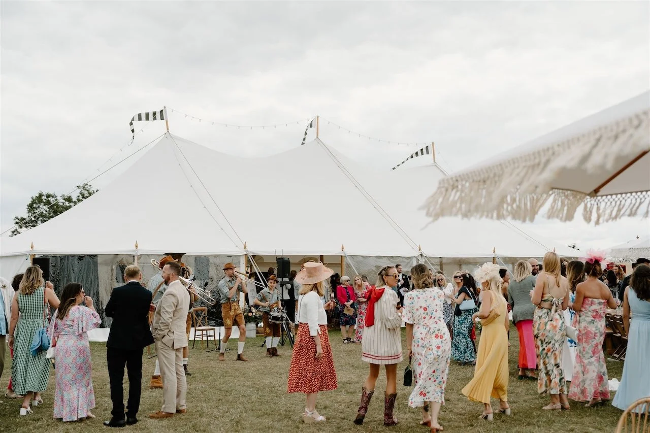 Oom Pah band playing in front of the marquee at Ed’s Hill Top festival-style wedding in Stamford, surrounded by colourfully dressed guests