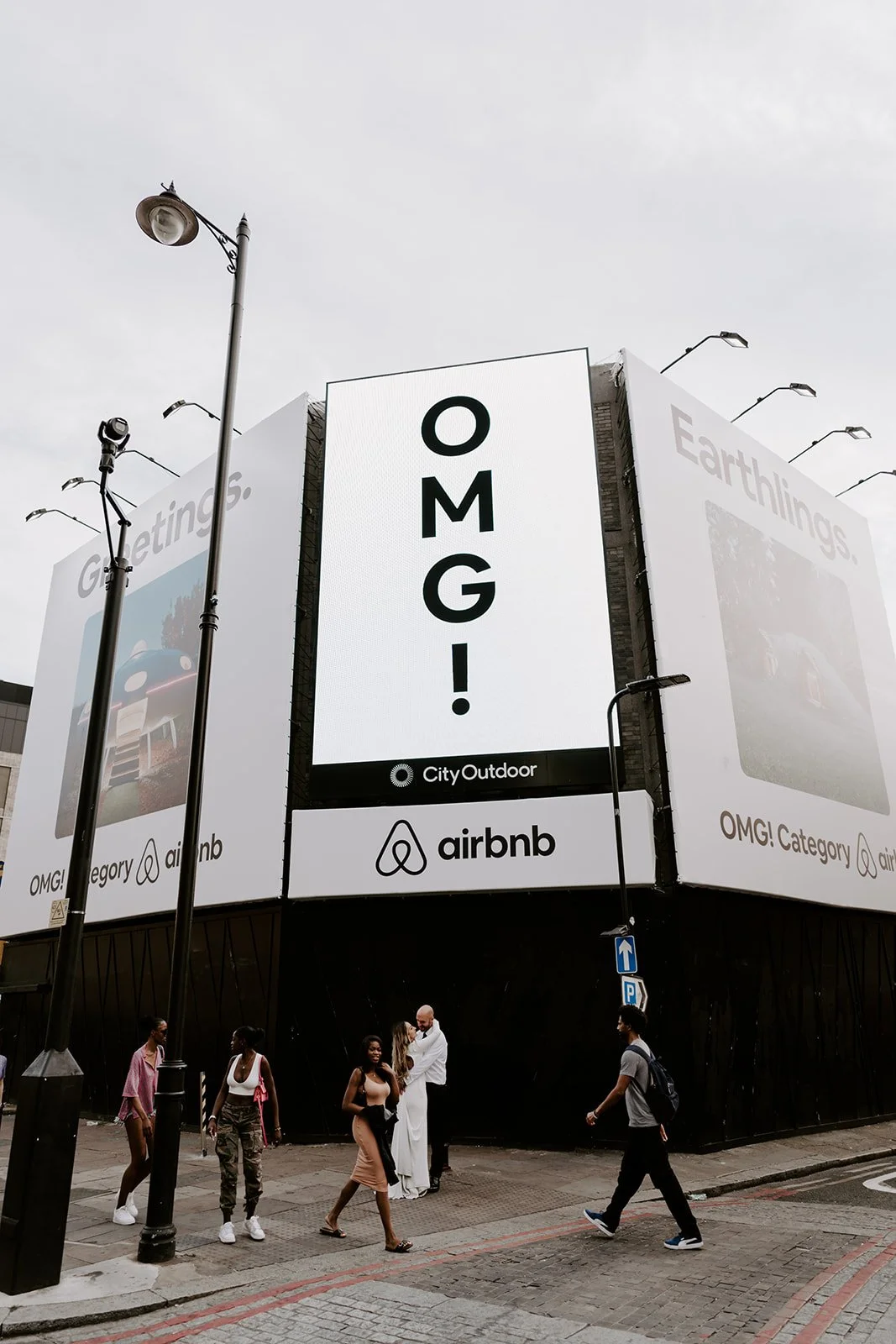 London wedding couple embracing under a huge OMG billboard while pedestrians walk past in Shoreditch