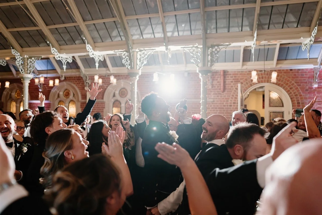 Guests dancing and singing together during a black tie wedding reception at Kilworth House, captured in a documentary style as the room fills with energy and light.