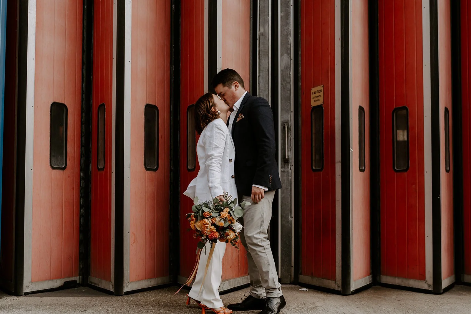 Bride and groom kissing in front of Angel Fire station doors during their London wedding portrait session