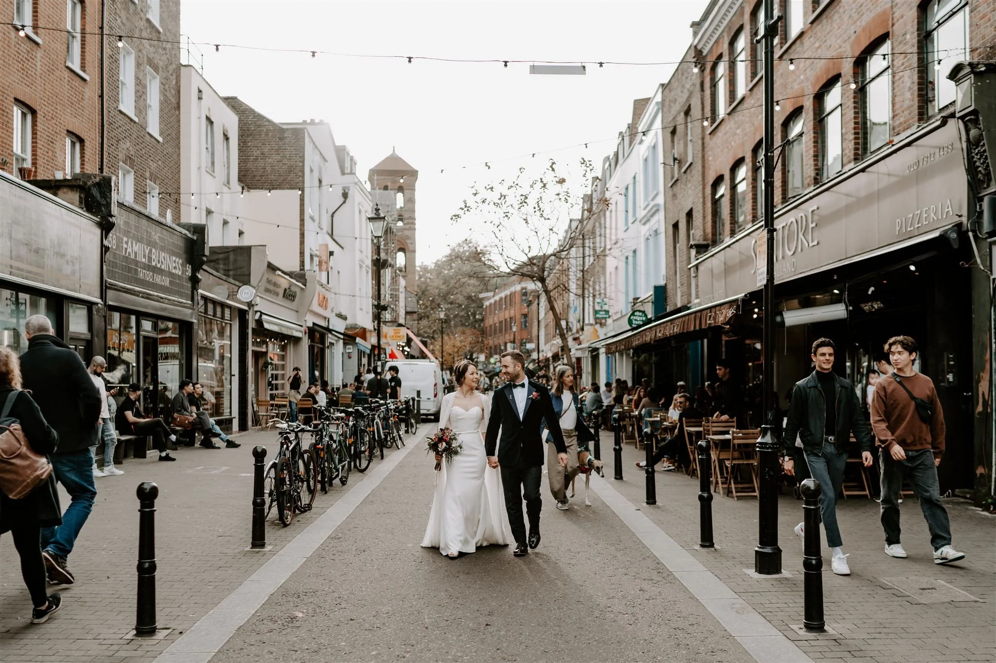 London town hall wedding couple walking through a busy East London street with people and cafés around them