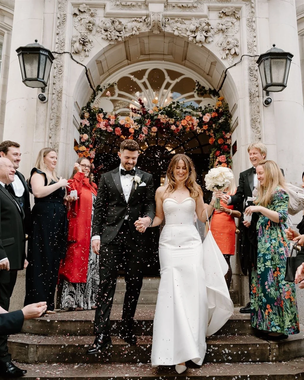 Bride and groom walking out of Chelsea Town Hall in London as guests throw confetti outside the ceremony.
